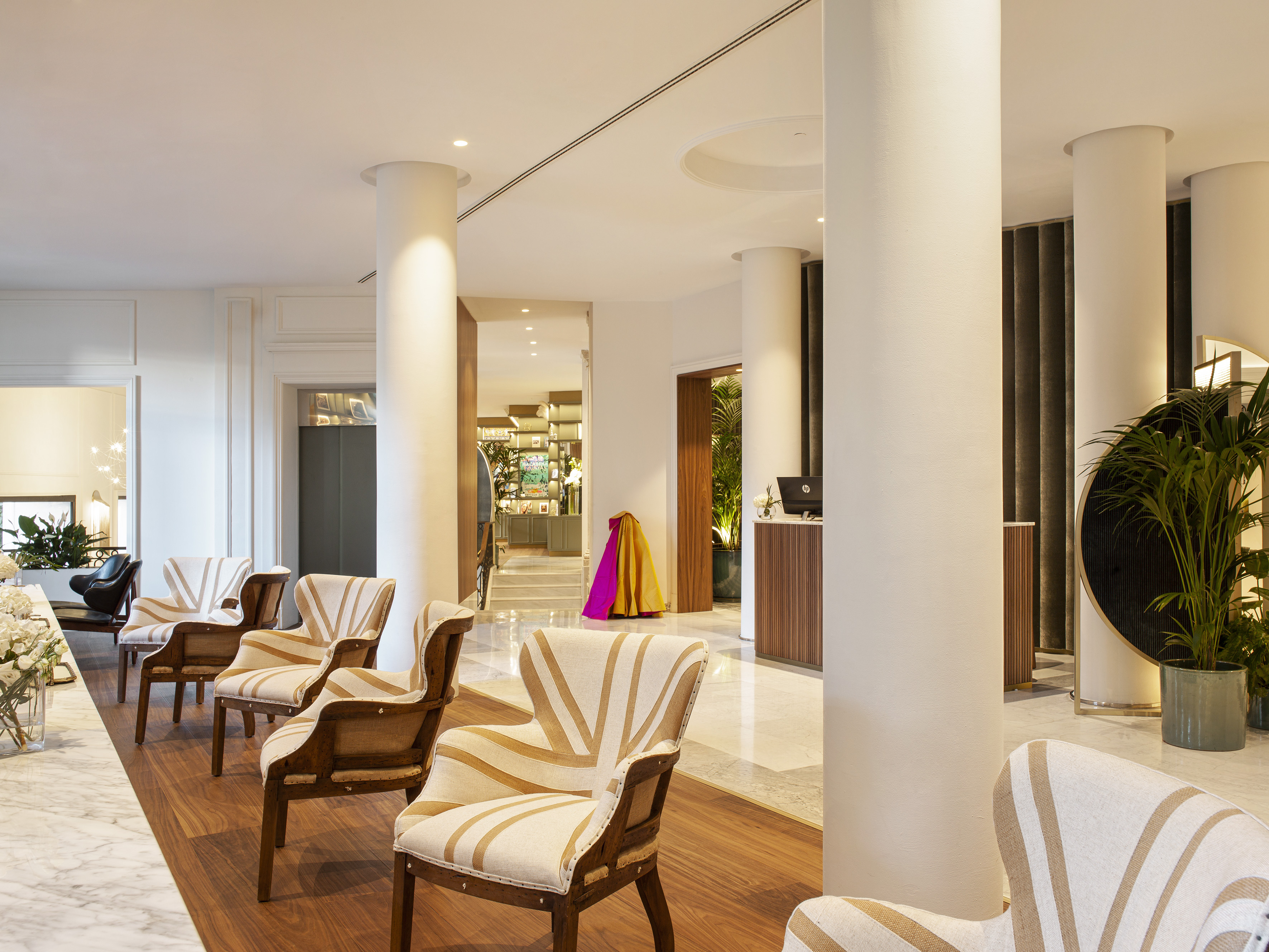 Hotel lobby with striped lounge chairs, white columns, and reception area.