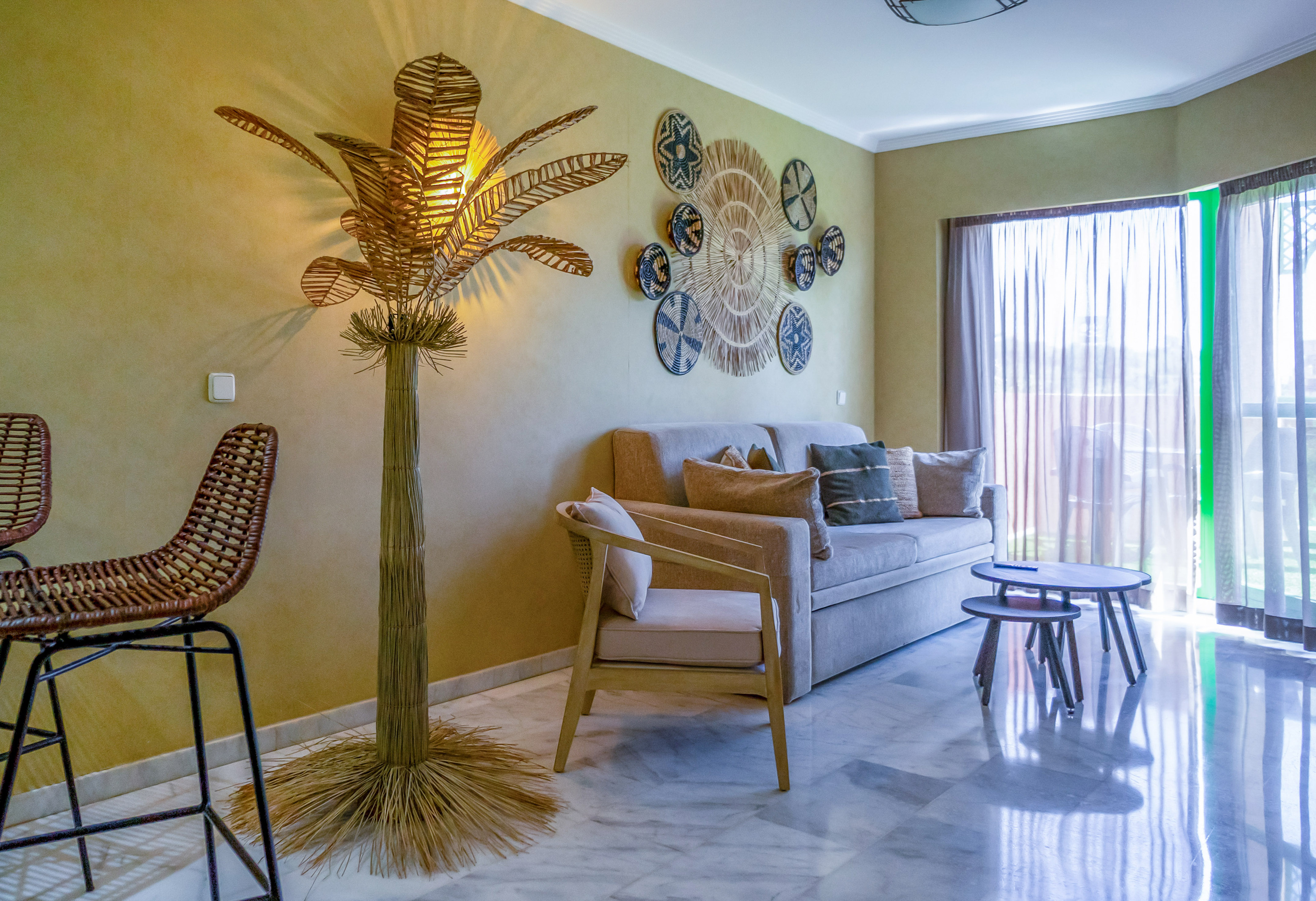 Boho living room with sofa, rattan lamp, woven wall art, and marble floor.