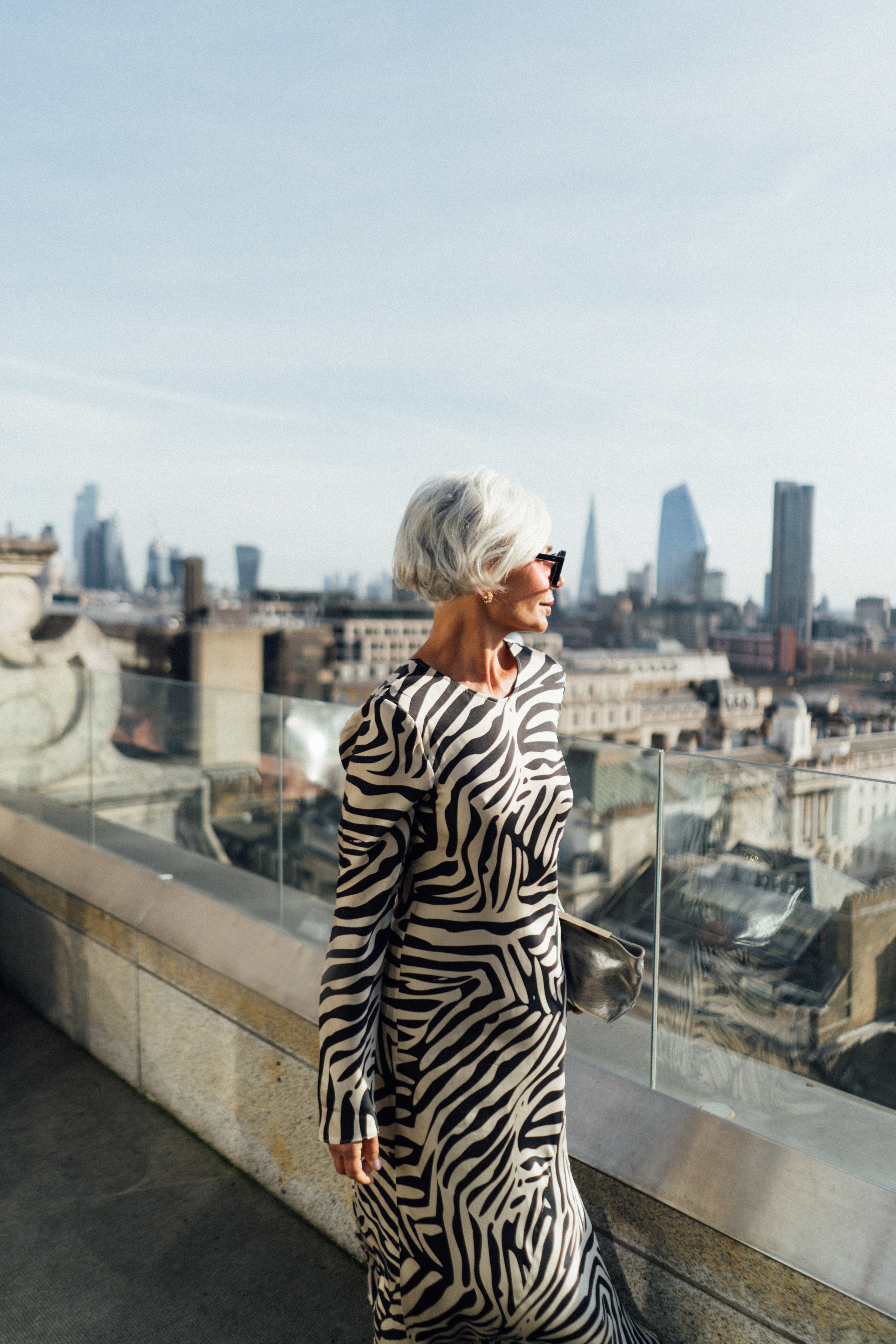 Stylish woman in zebra print dress and sunglasses on London rooftop, cityscape view.