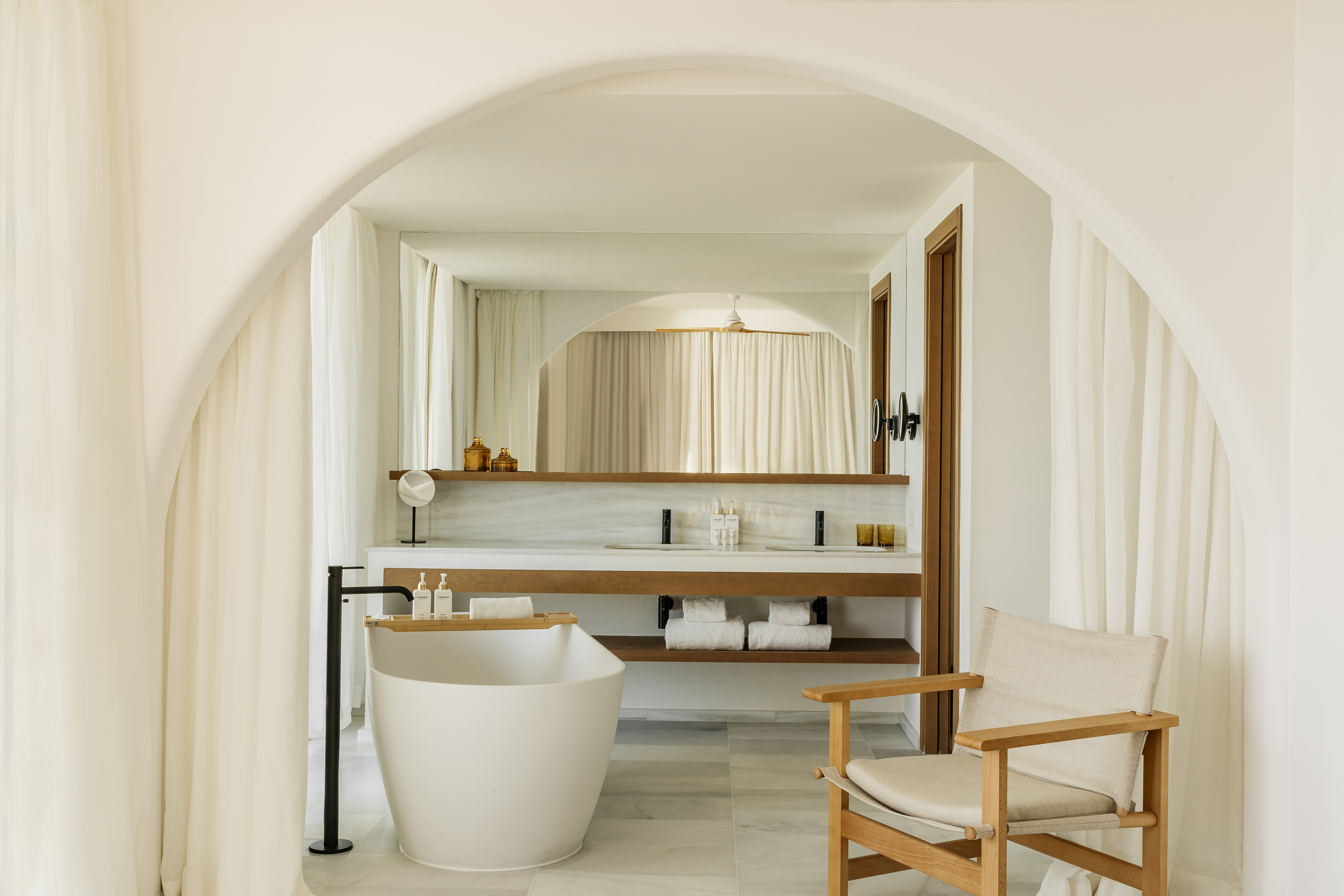 Modern minimalist bathroom with freestanding tub, double vanity, and arch.