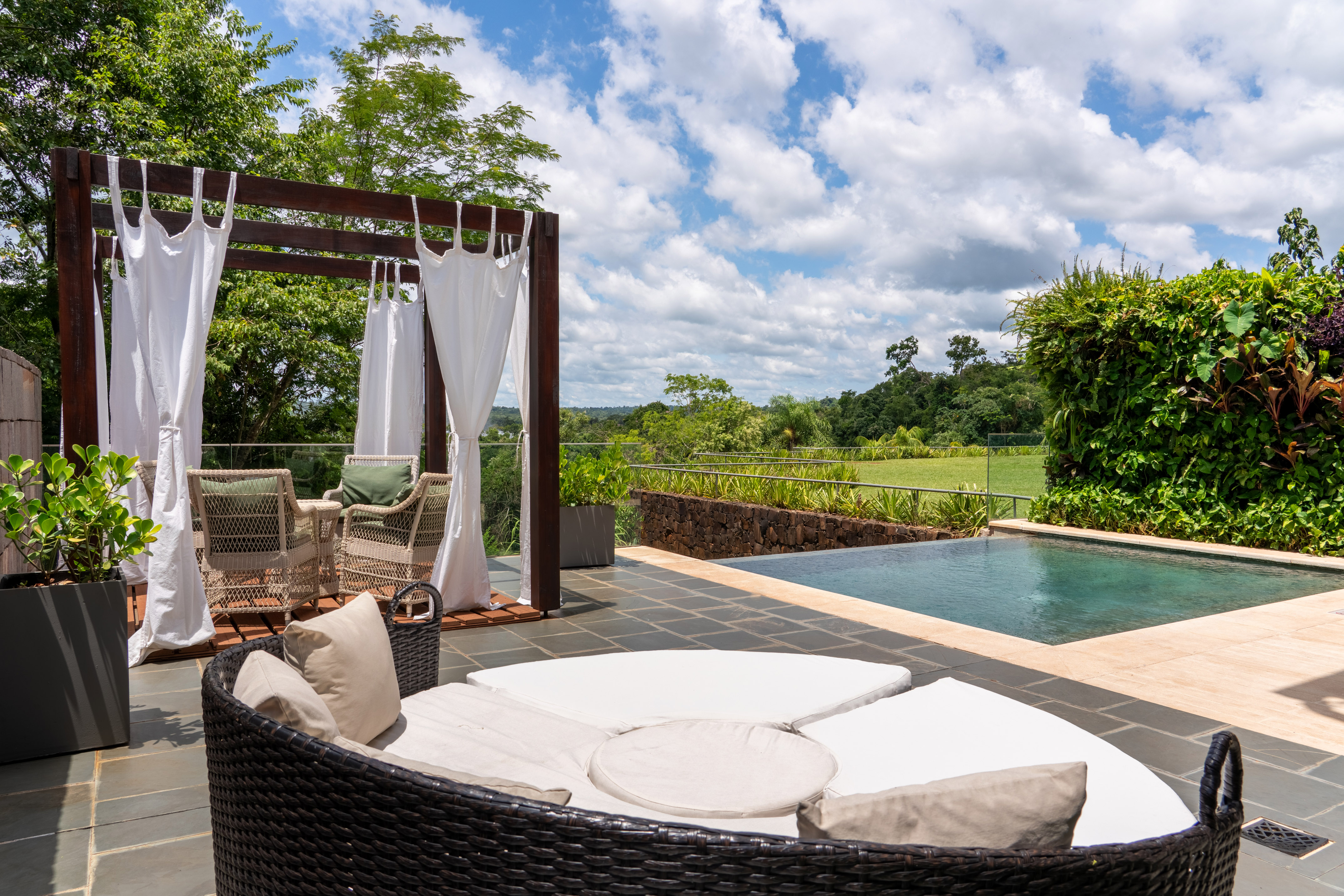 Relaxing patio with pool, round daybed, pergola, and green jungle view.