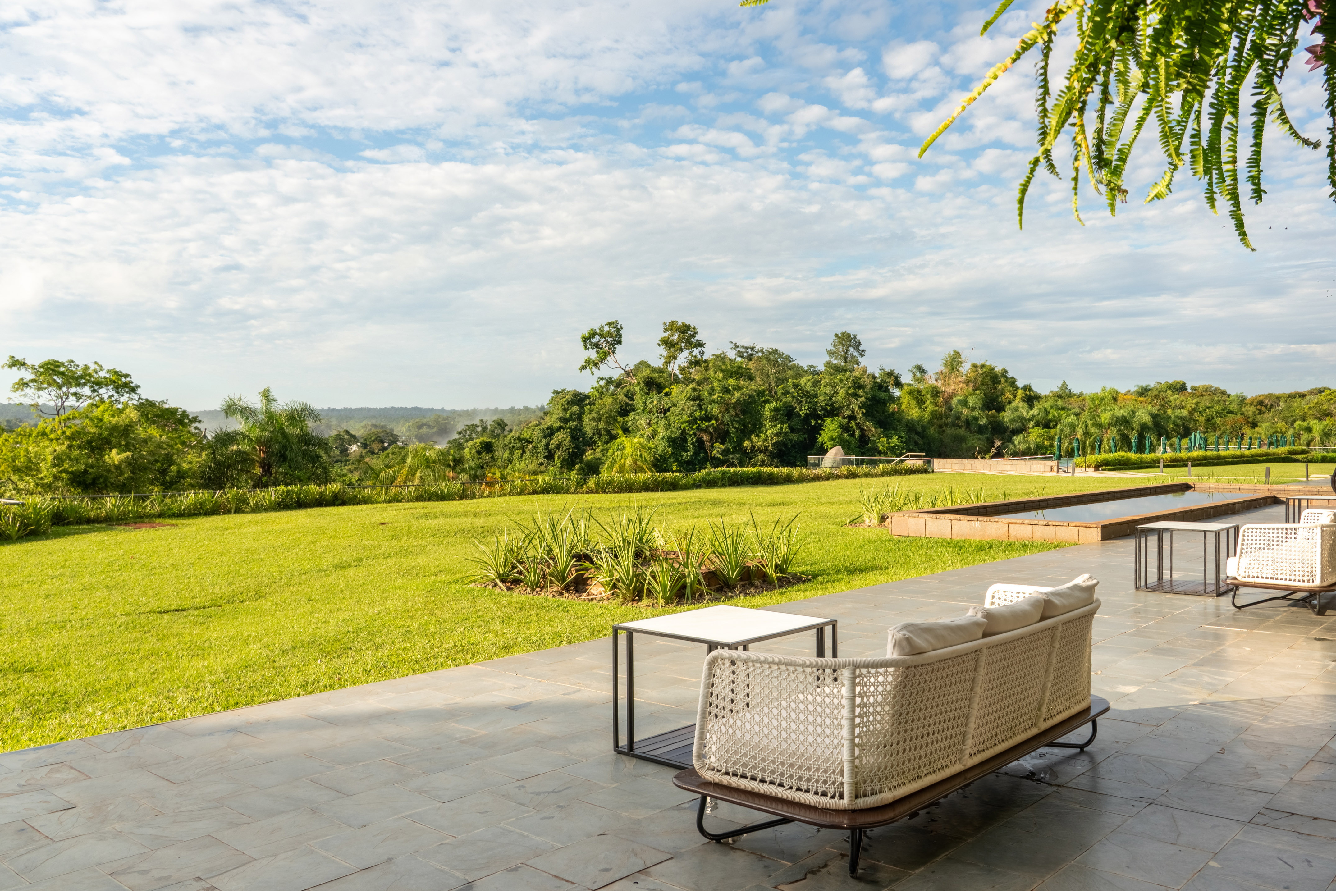 Outdoor patio with sofa overlooking green lawn, tropical trees, and resort pool.