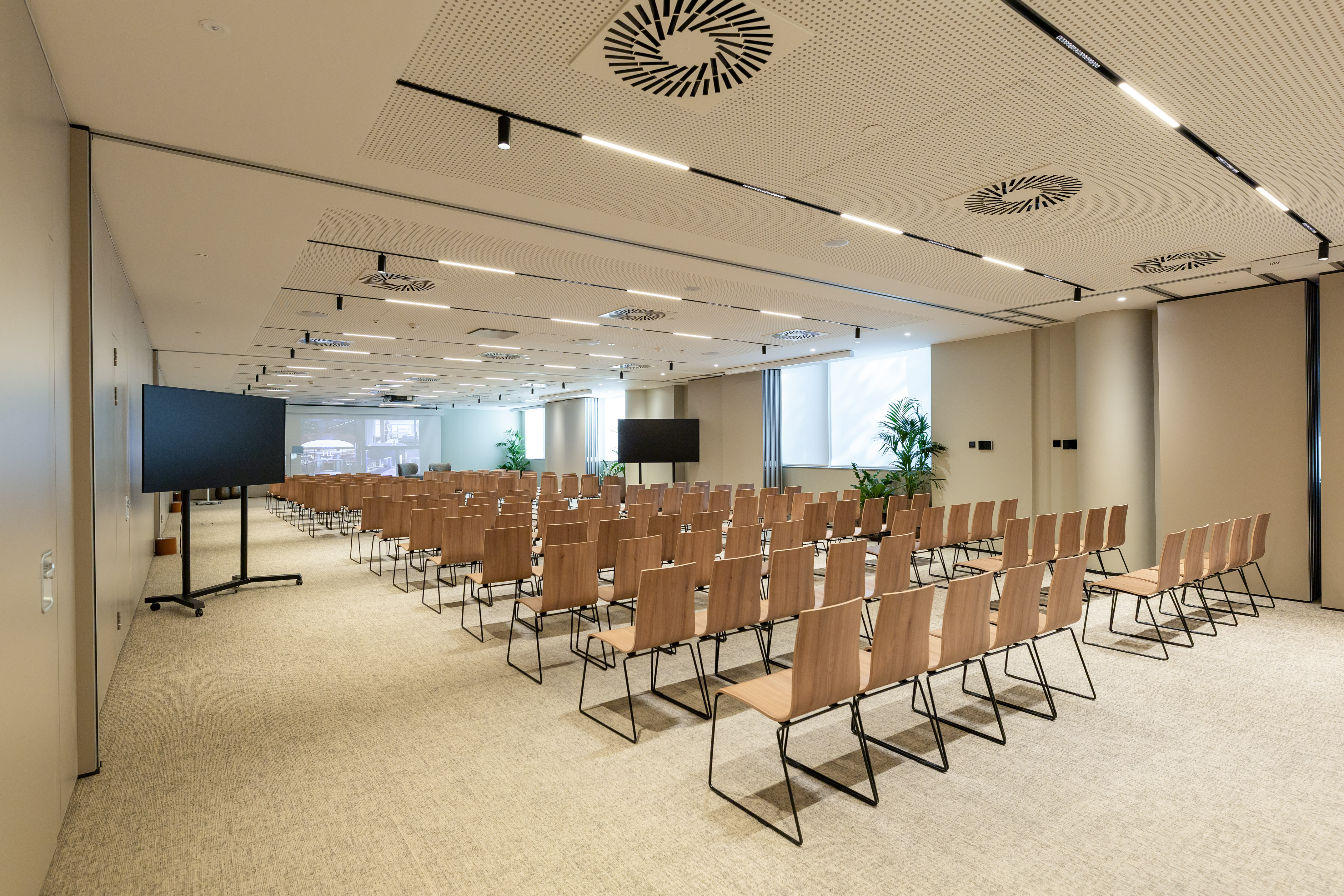 Modern empty conference room with rows of chairs, large screens, and projector.