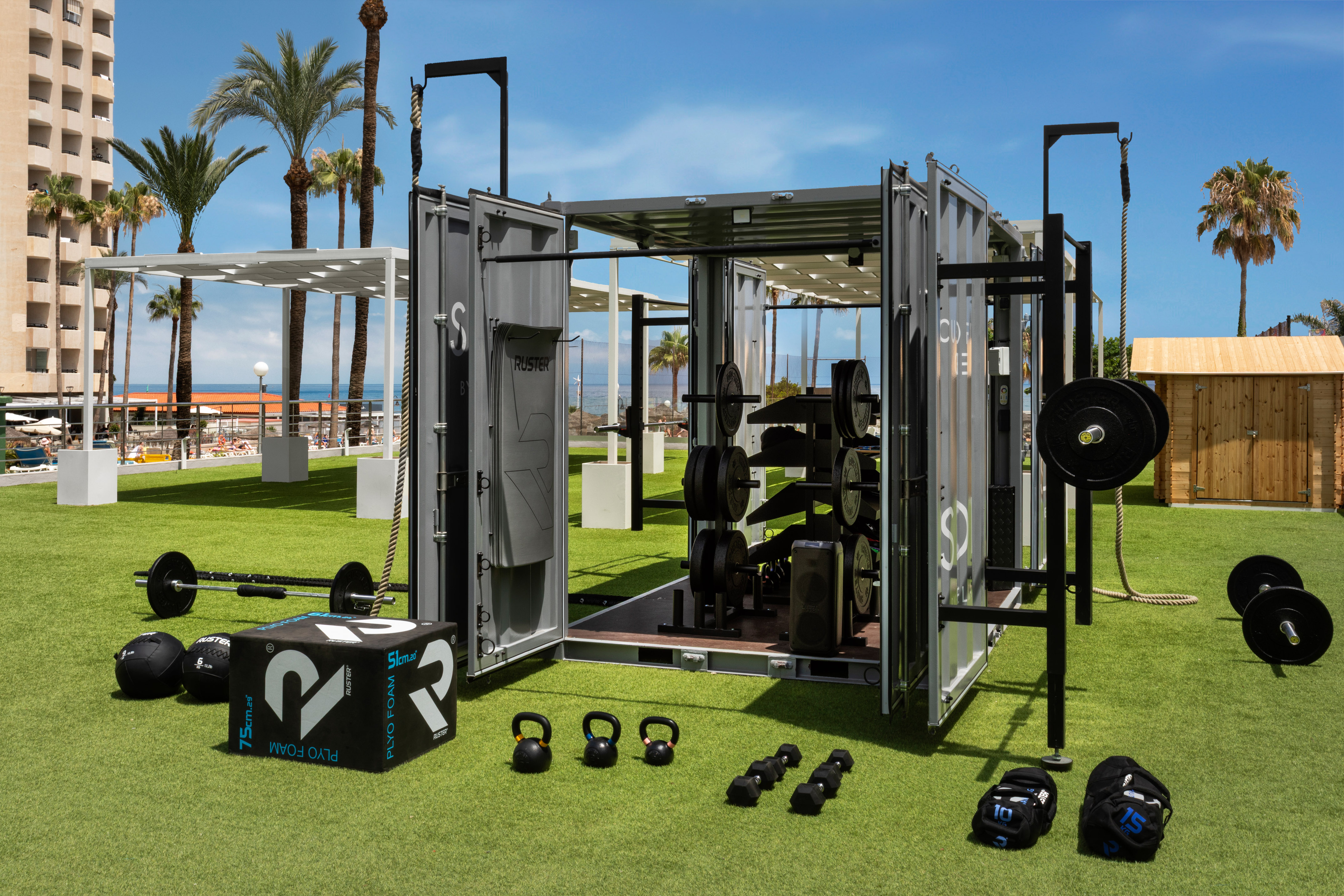 Ruster outdoor container gym with fitness equipment on grass, beach background.