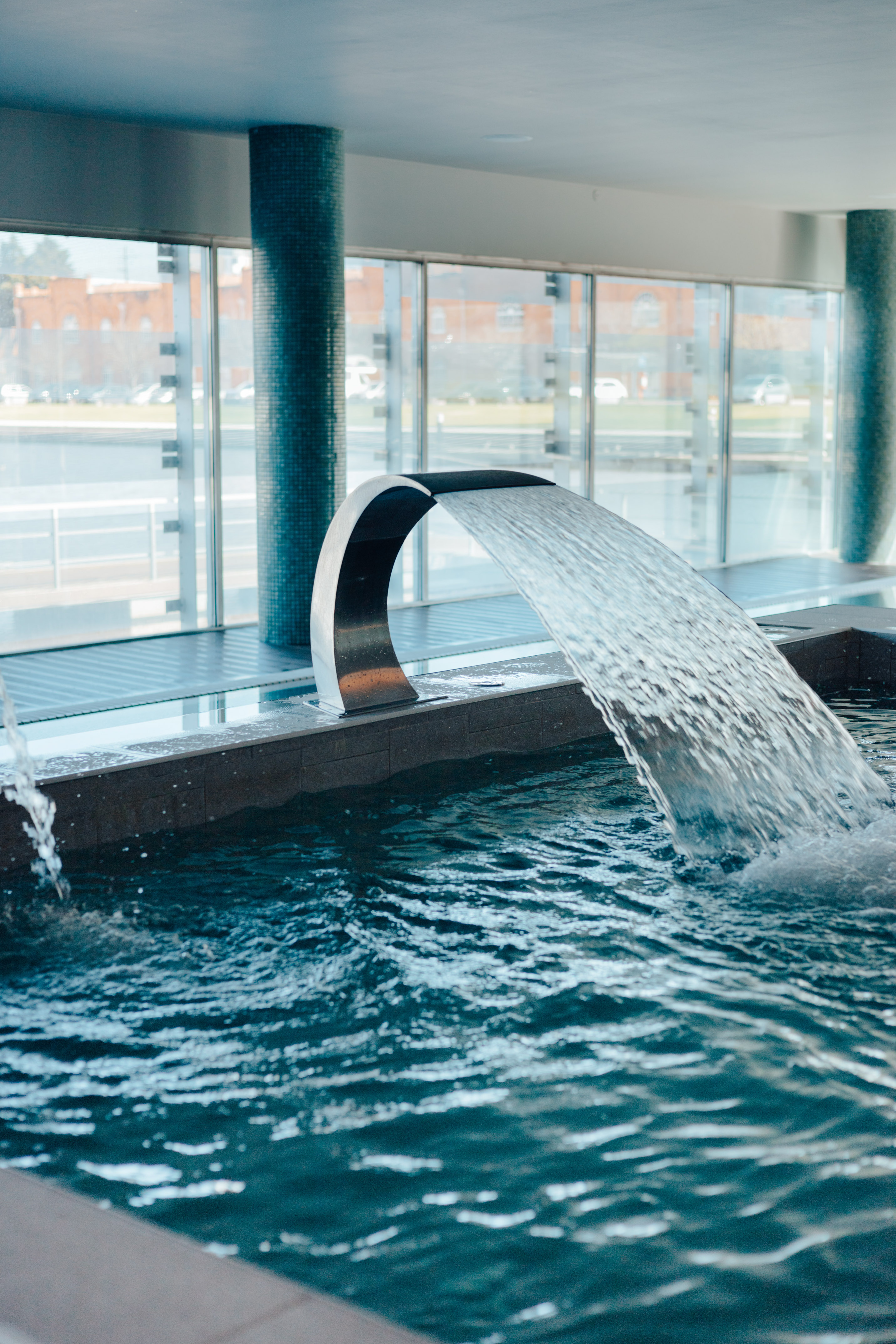 Piscina interior moderna con chorro de agua en spa, ventanales panorámicos.