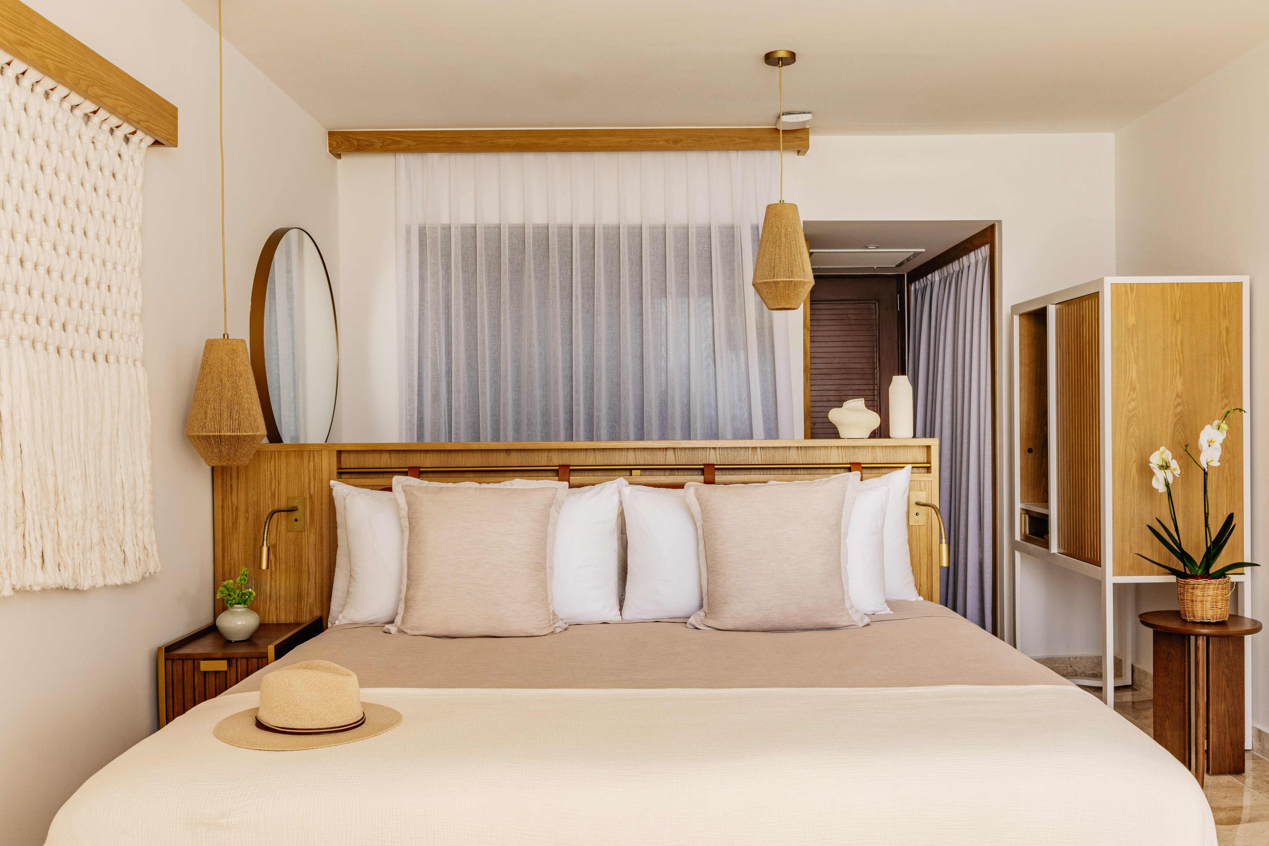 Bright, modern bedroom with neutral decor, wood headboard, macrame, woven lights.