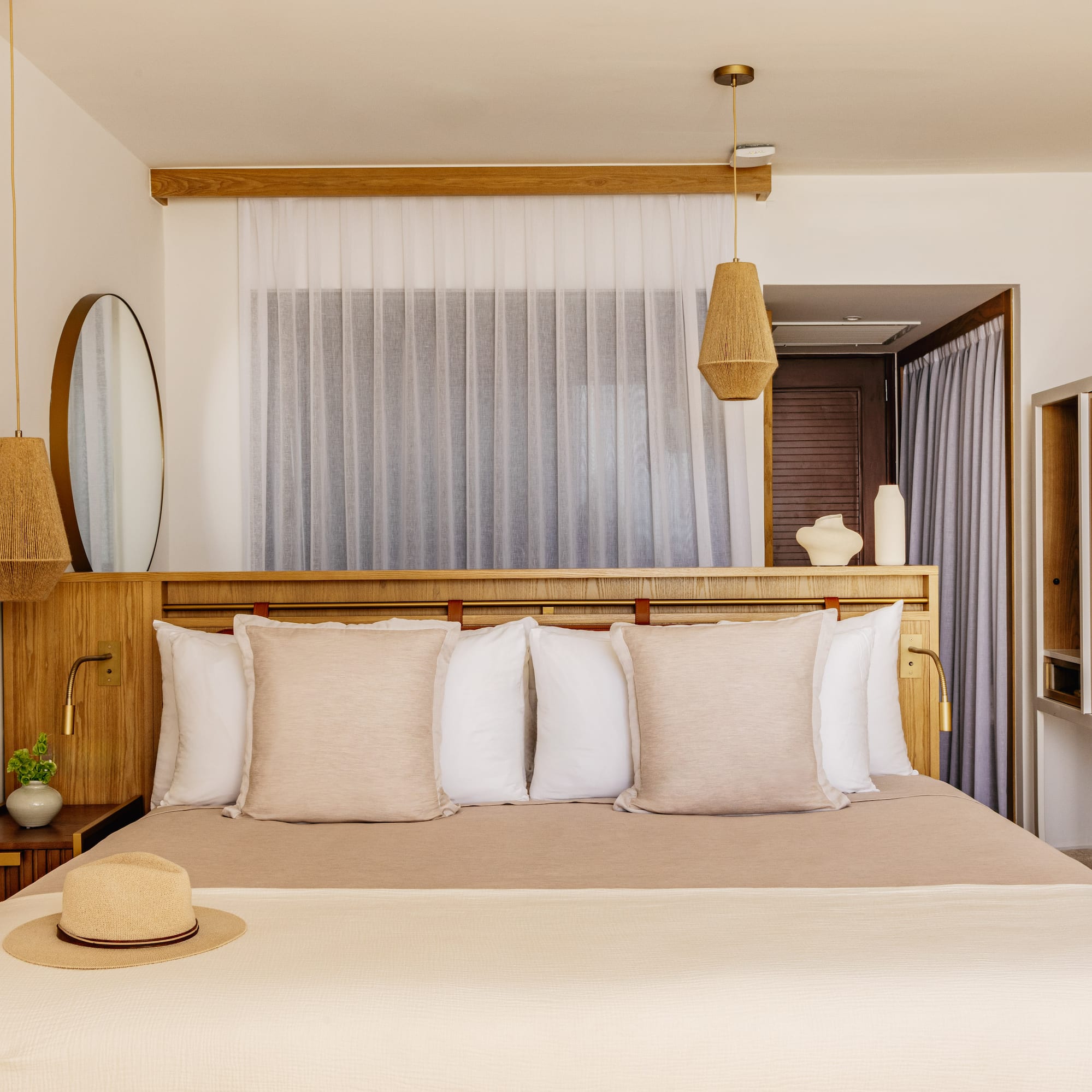 Bright, modern bedroom with neutral decor, wood headboard, macrame, woven lights.