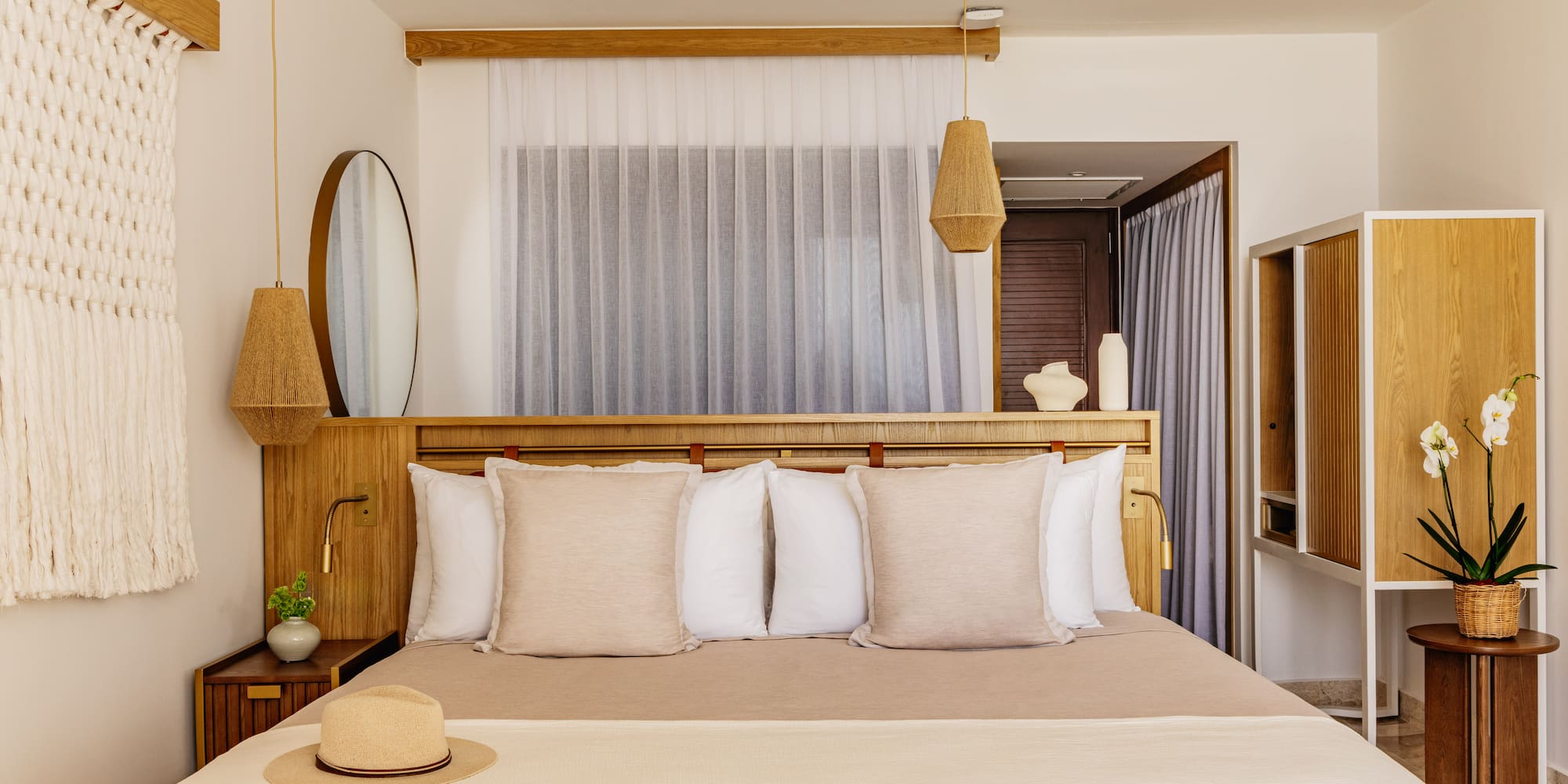 Bright, modern bedroom with neutral decor, wood headboard, macrame, woven lights.