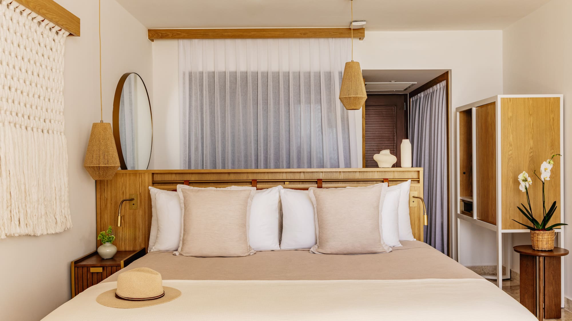 Bright, modern bedroom with neutral decor, wood headboard, macrame, woven lights.