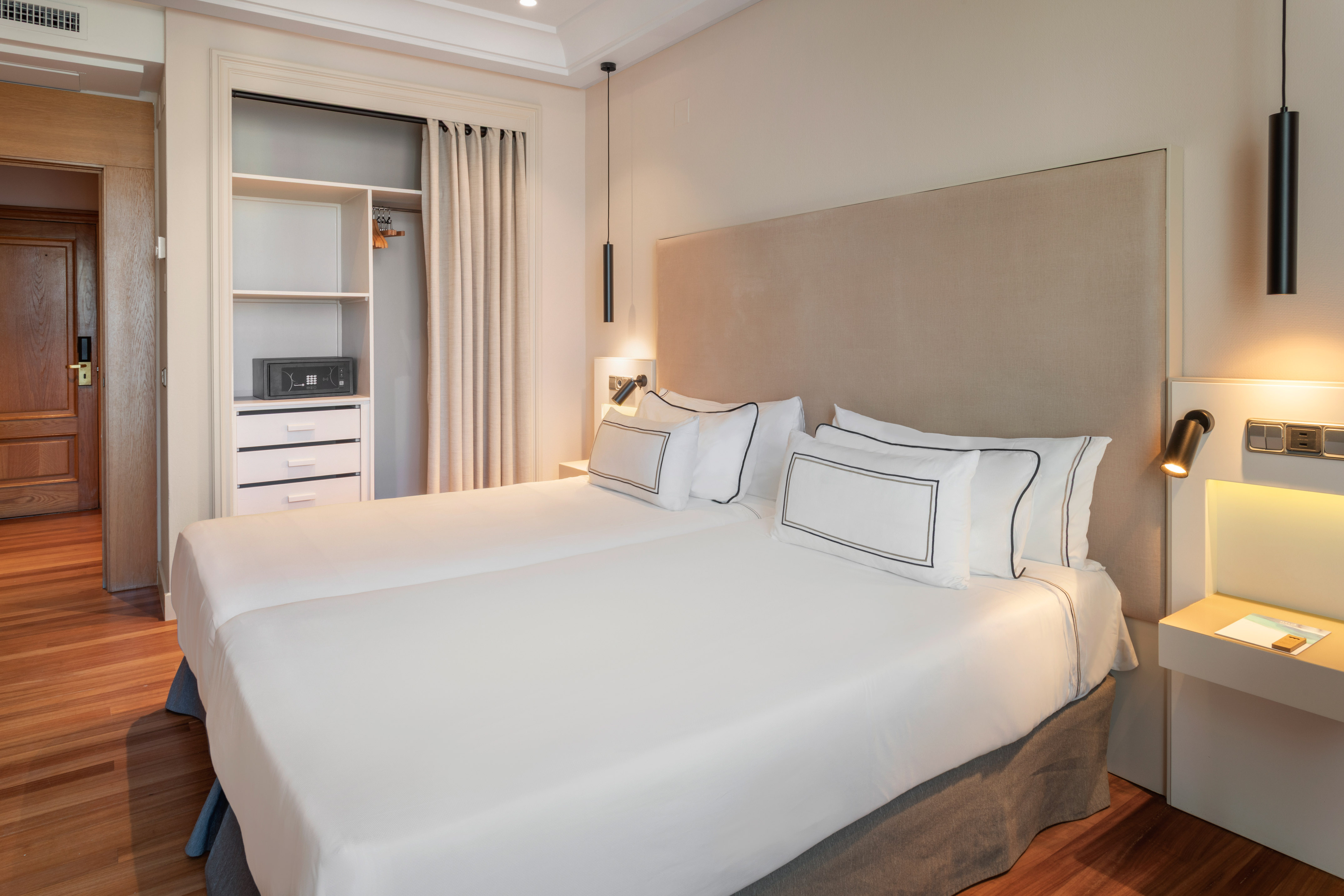 Hotel room with twin beds, white bedding, wood floor, and closet safe.
