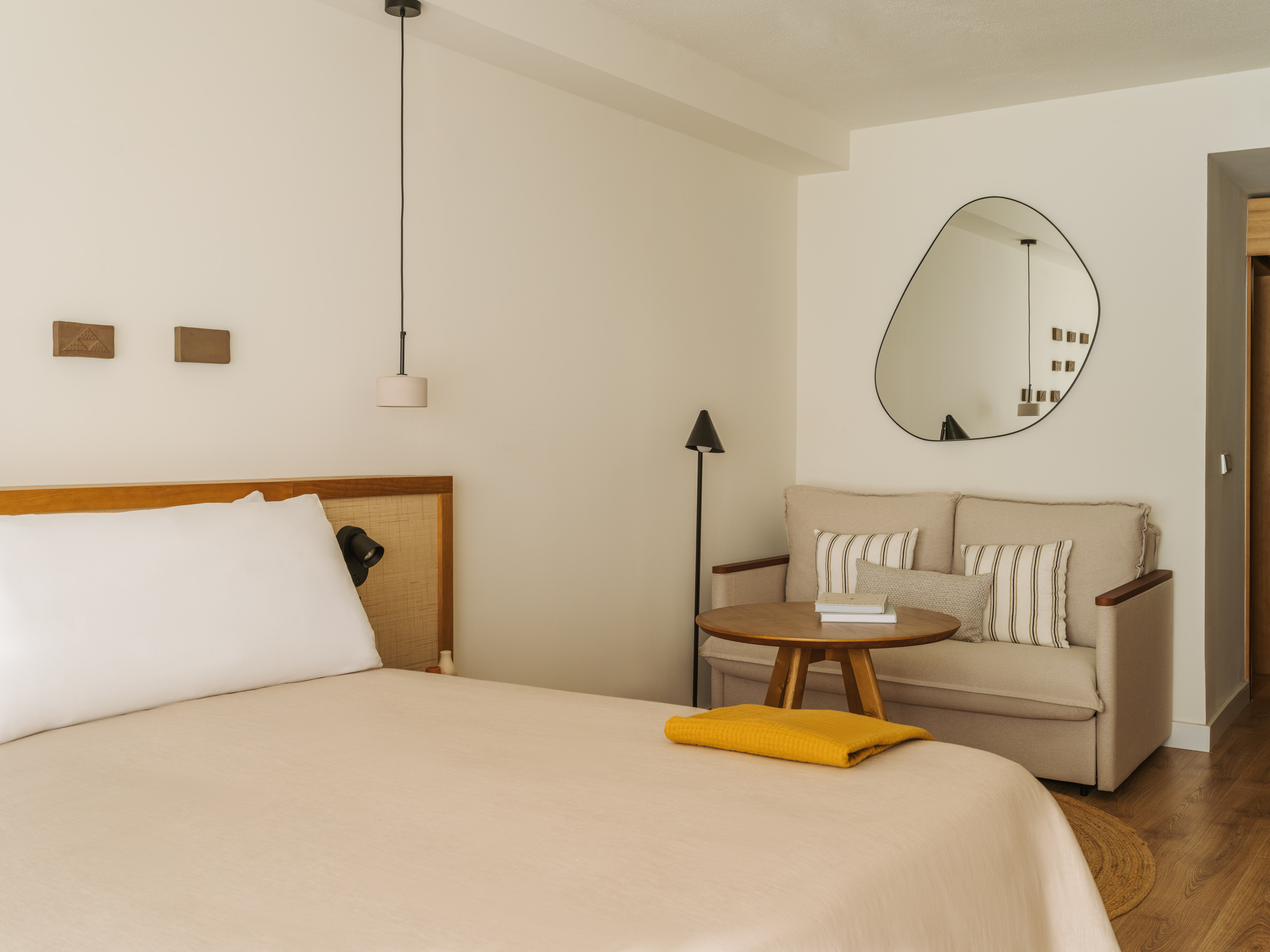 Contemporary bedroom with beige bed, sofa, wooden table, and abstract mirror.