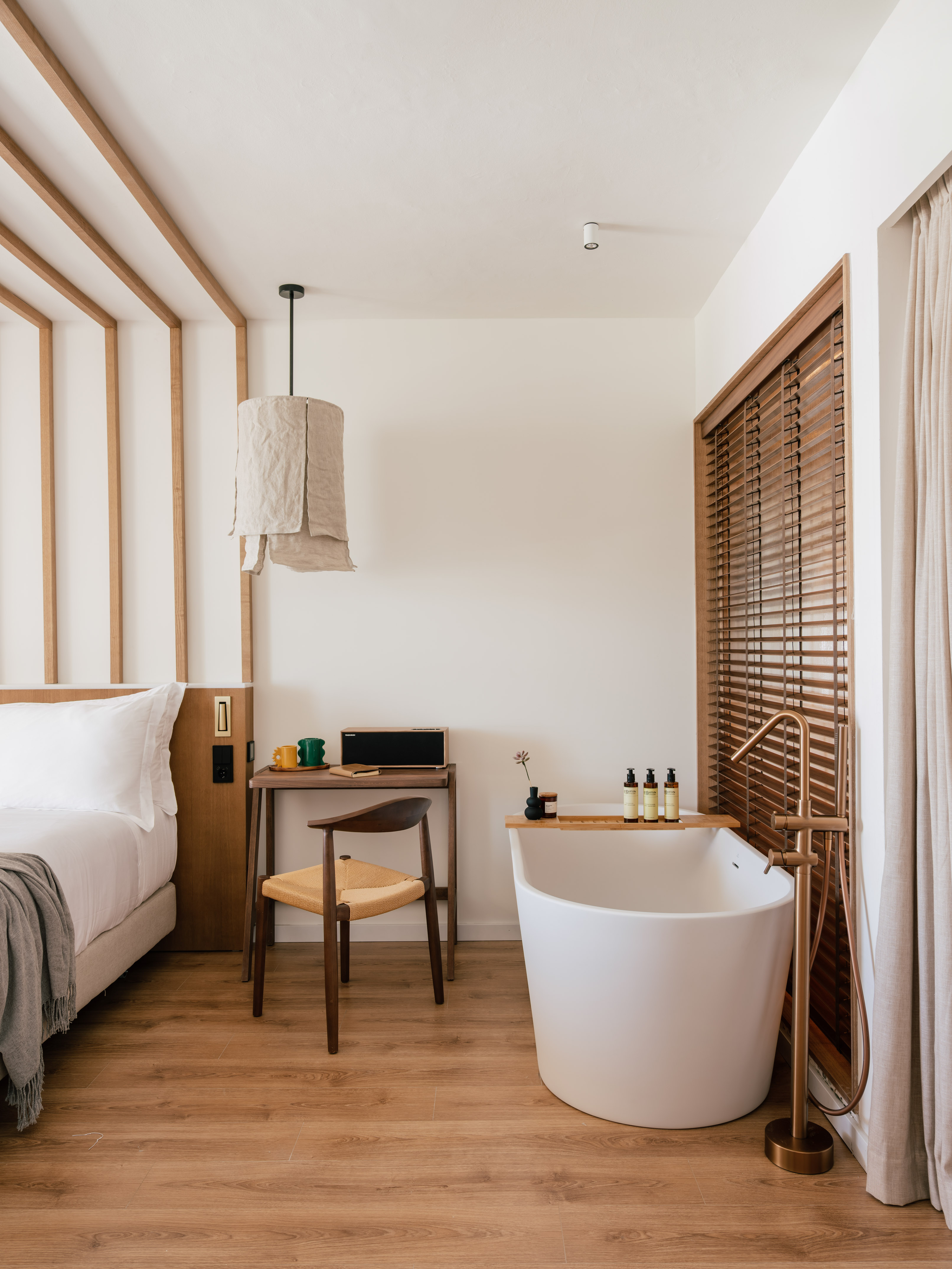 Modern spa-like hotel room with wooden bed, desk, and freestanding bathtub.