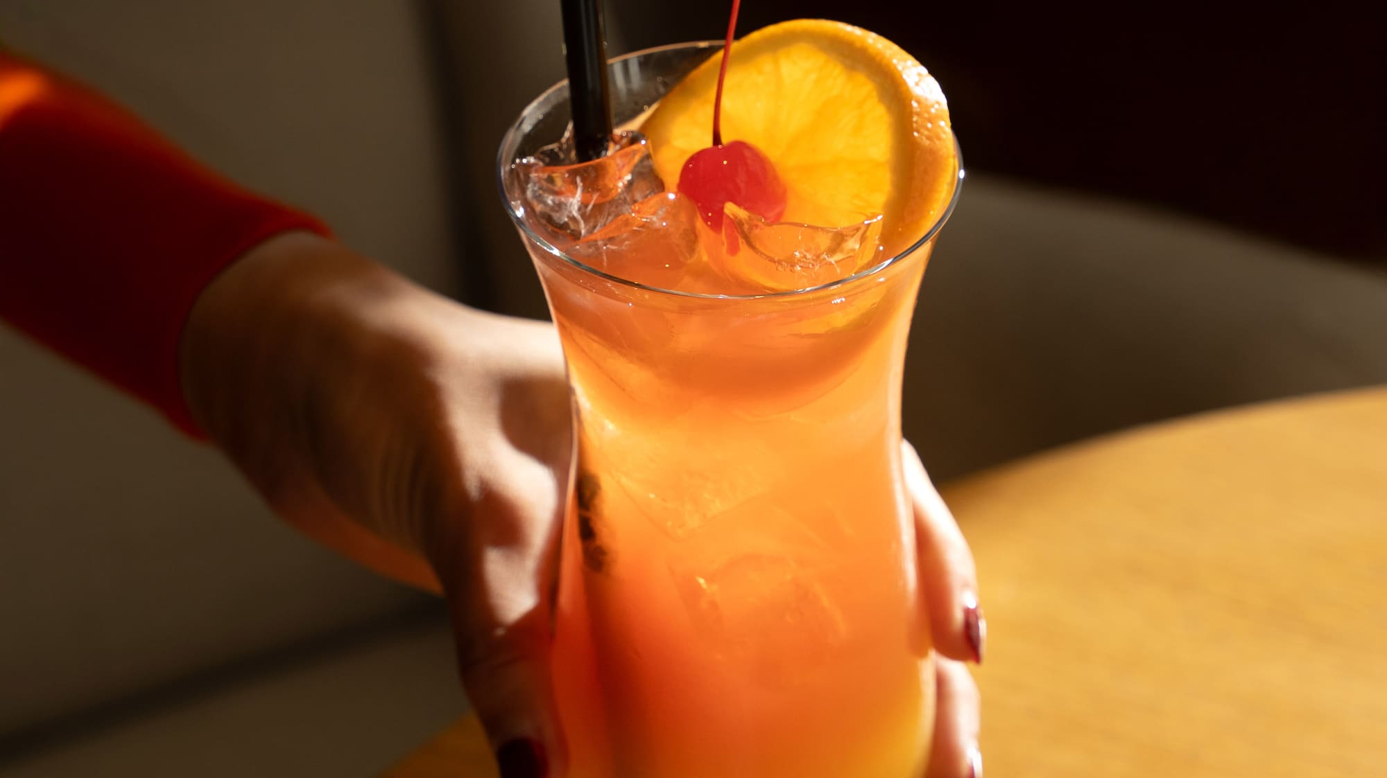 a hand holding a glass of orange juice with a straw