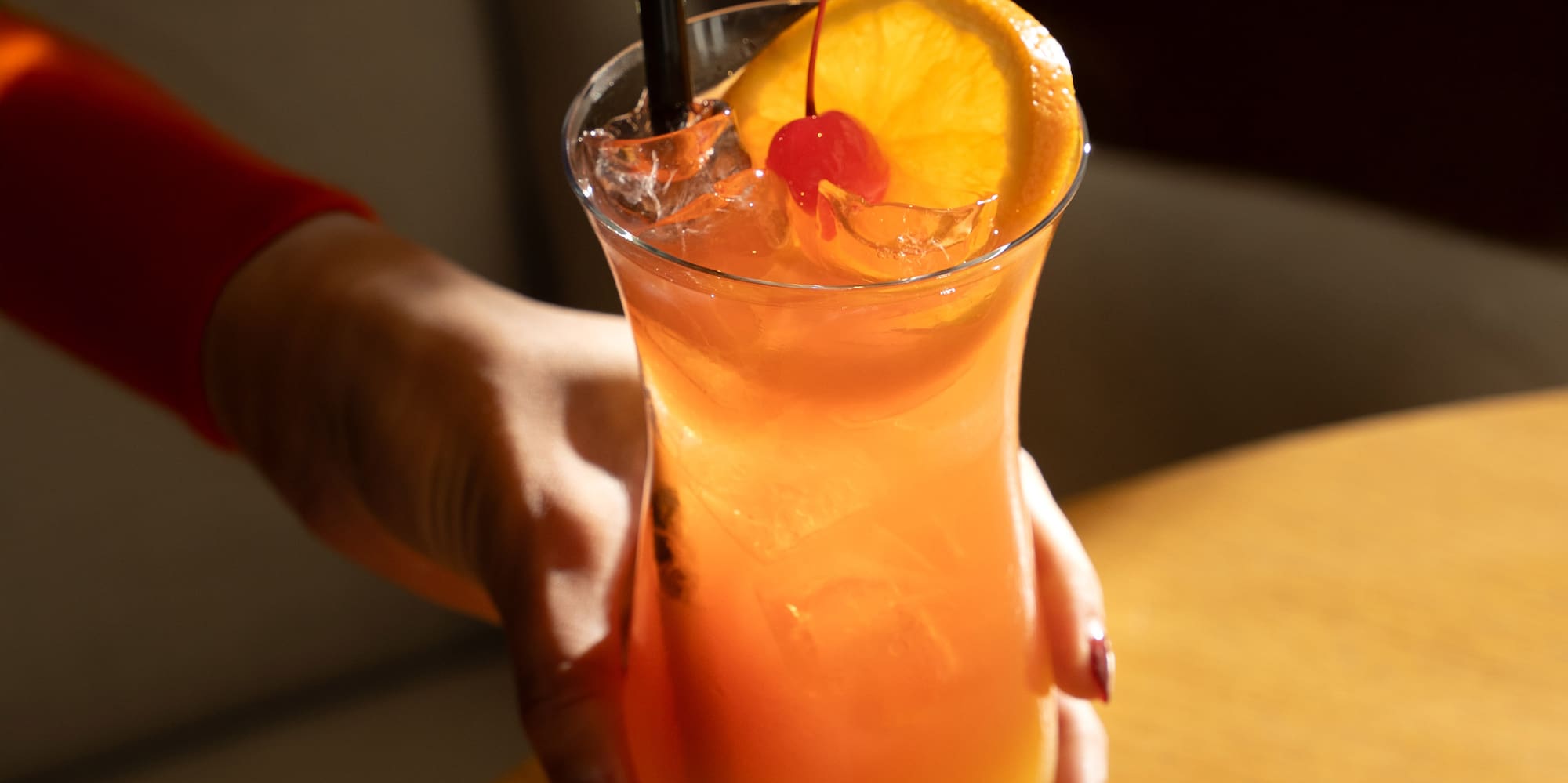 a hand holding a glass of orange juice with a straw