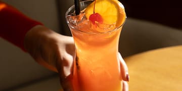 a hand holding a glass of orange juice with a straw
