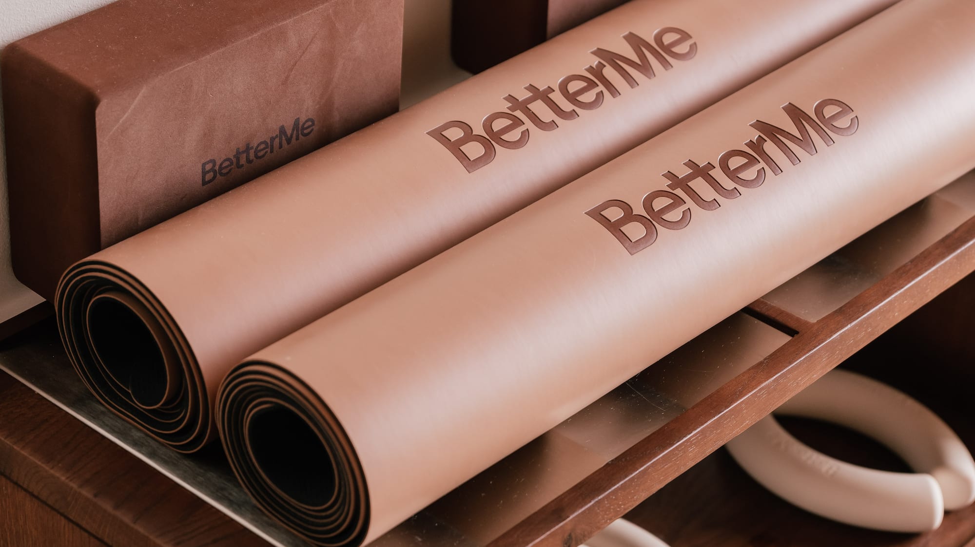 BetterMe yoga mats, blocks, and hand weights on a wooden shelf.