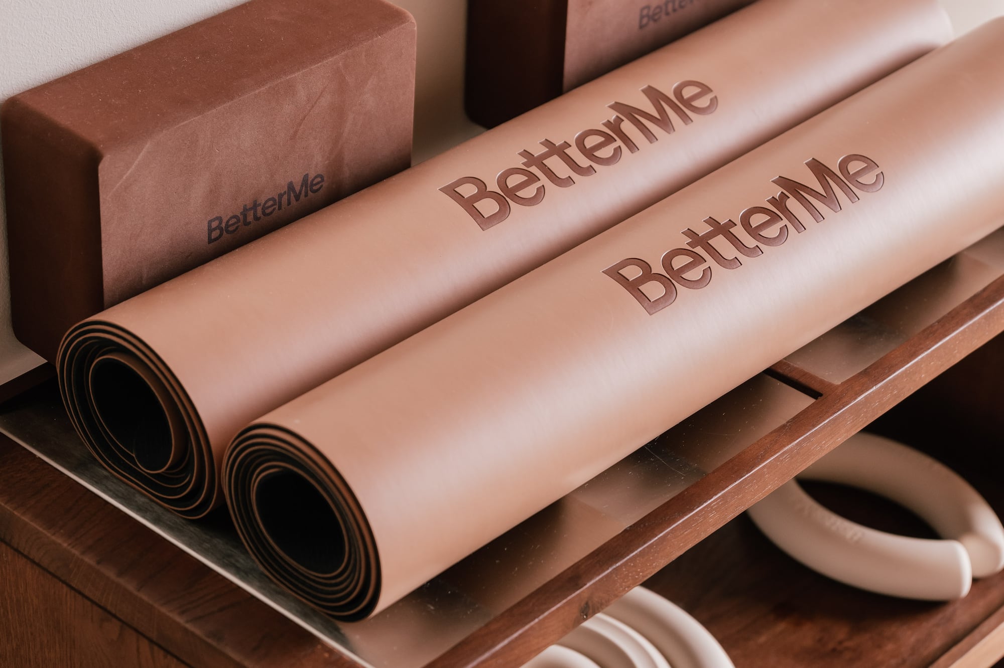 BetterMe yoga mats, blocks, and hand weights on a wooden shelf.