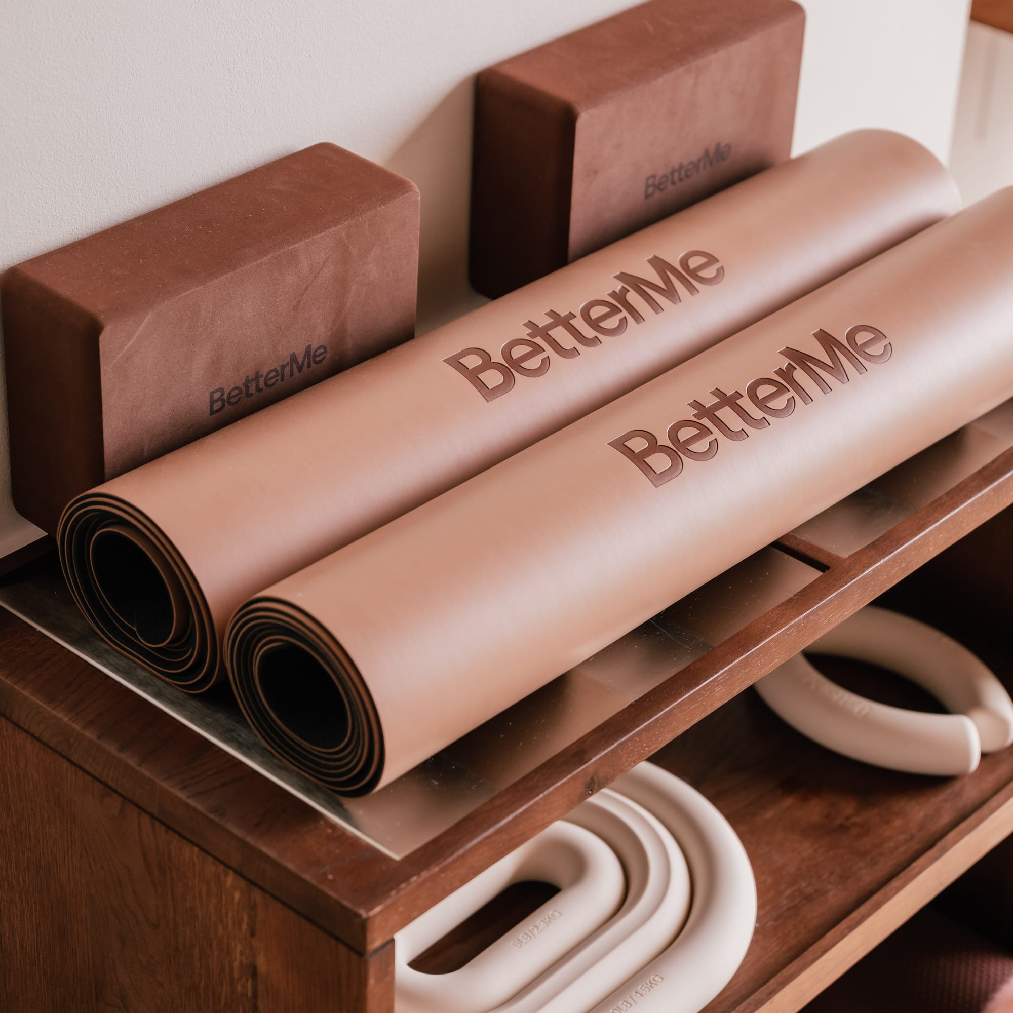 BetterMe yoga mats, blocks, and hand weights on a wooden shelf.