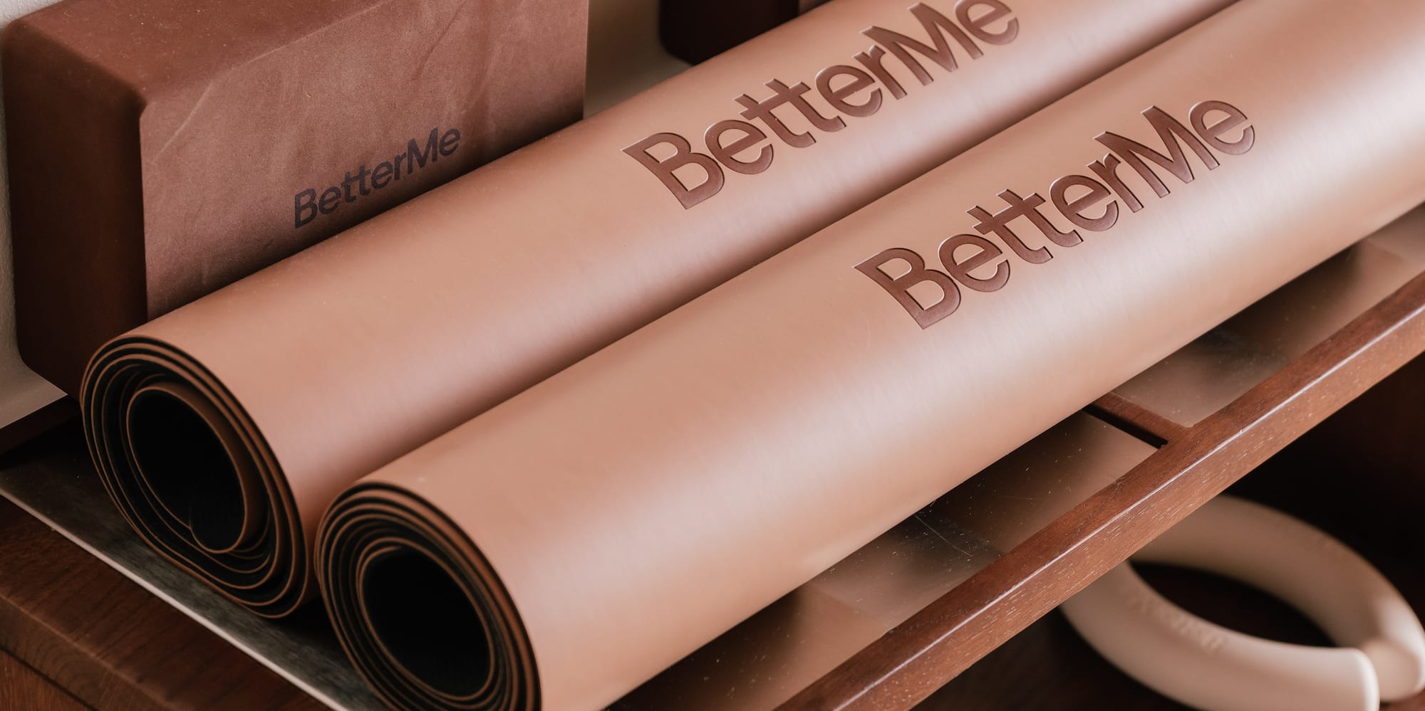 BetterMe yoga mats, blocks, and hand weights on a wooden shelf.