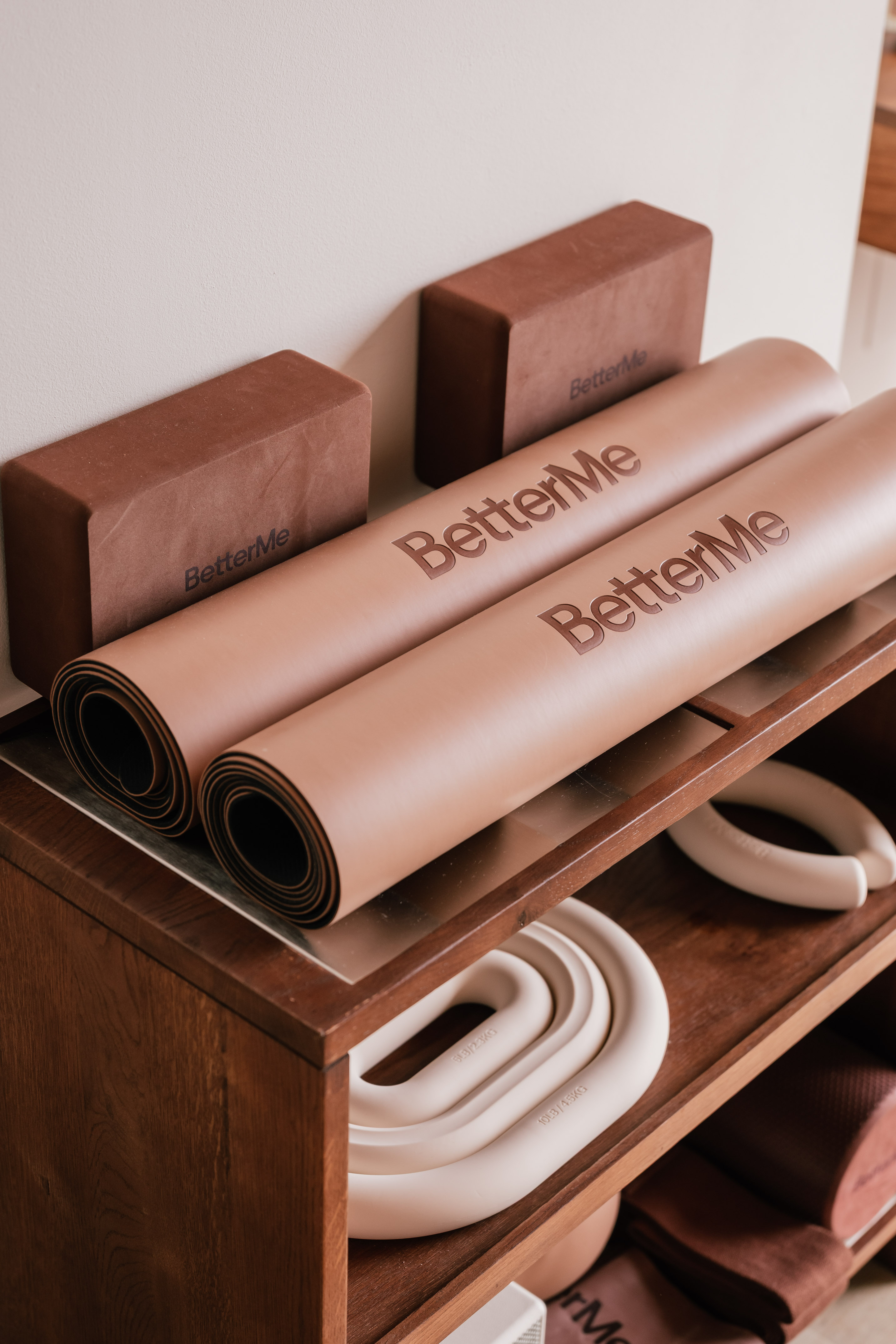 BetterMe yoga mats, blocks, and hand weights on a wooden shelf.