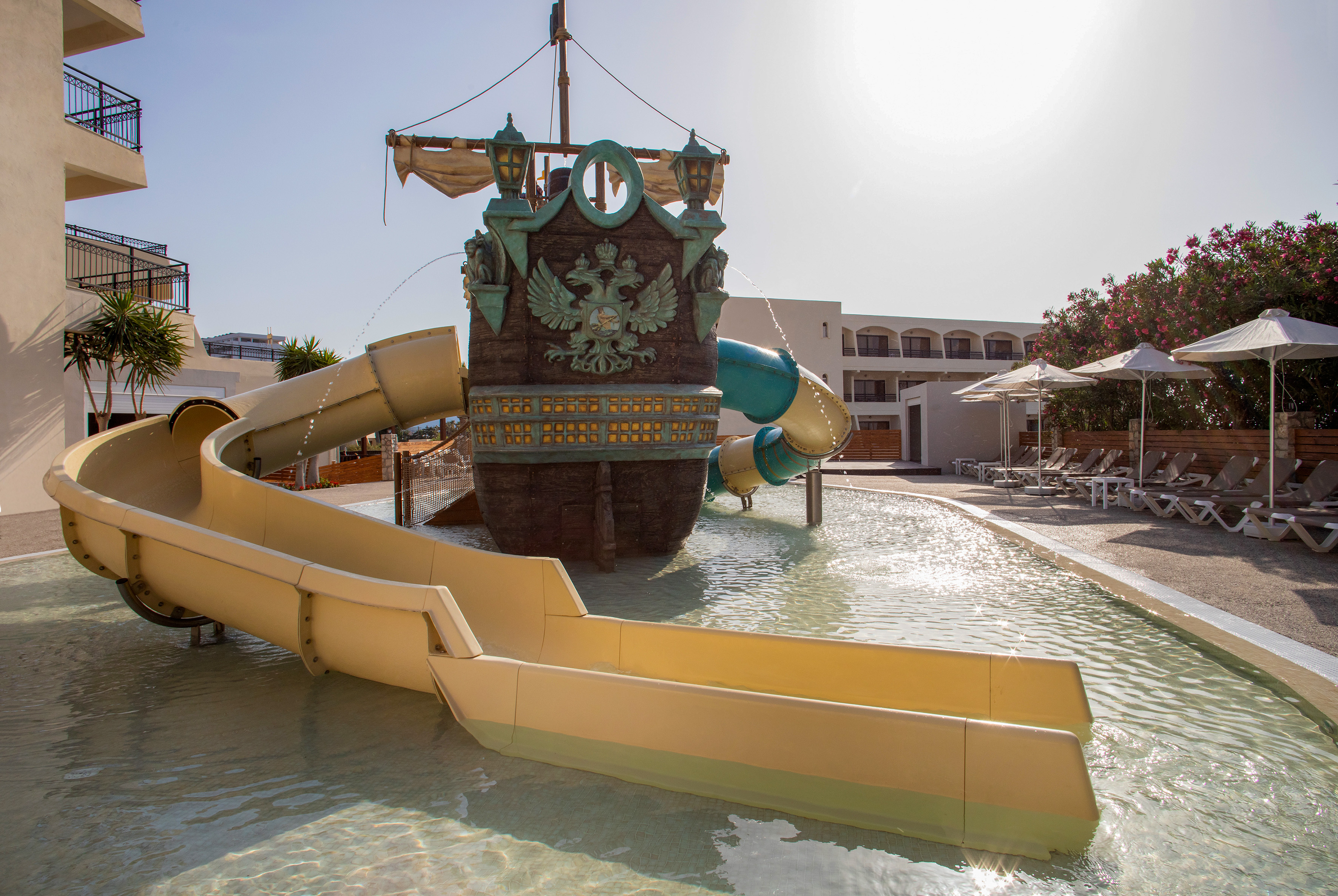 Pirate ship water slide with yellow slides in a sunny resort pool.