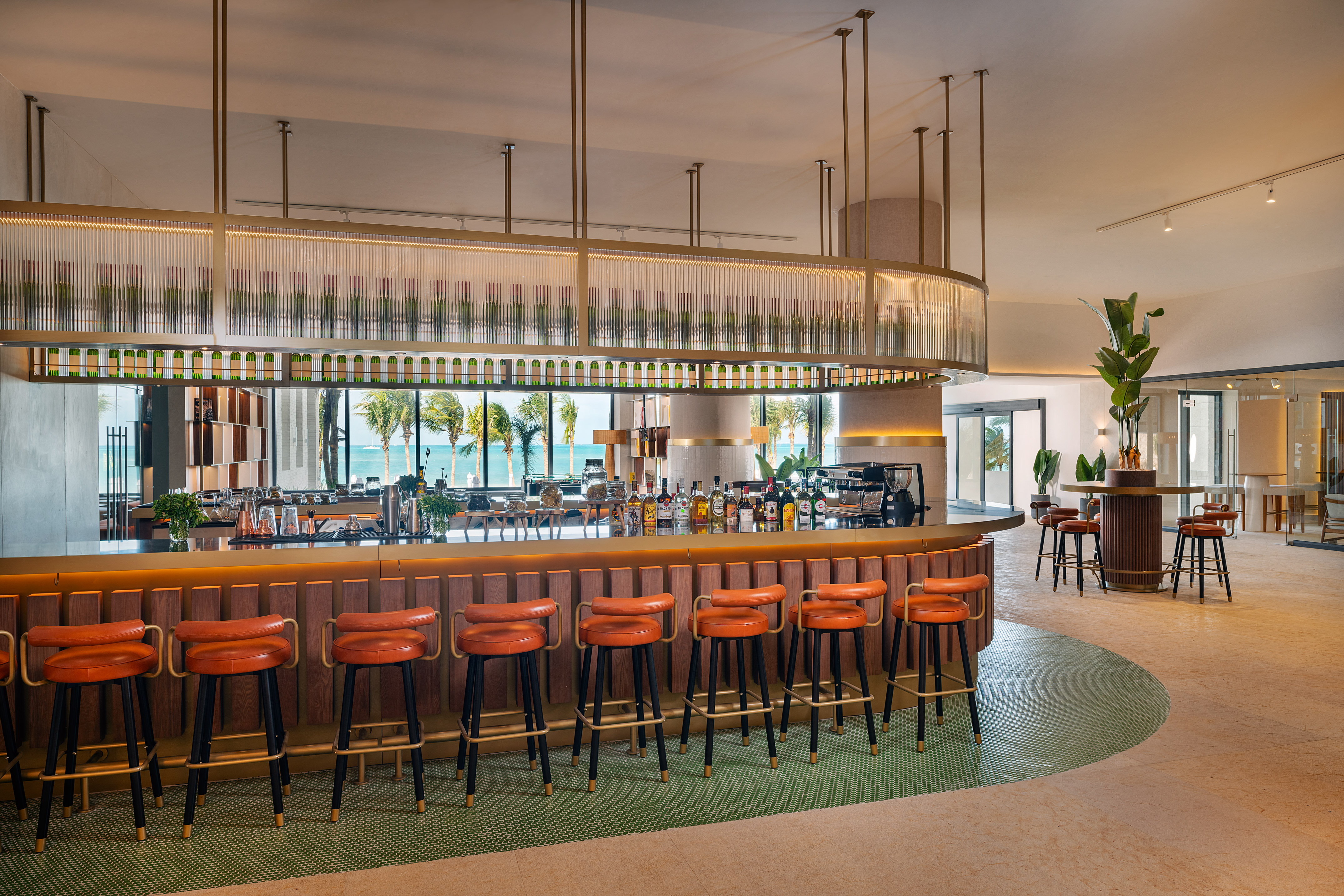 Modern bar with ocean view, sleek bottle display, and orange stools.