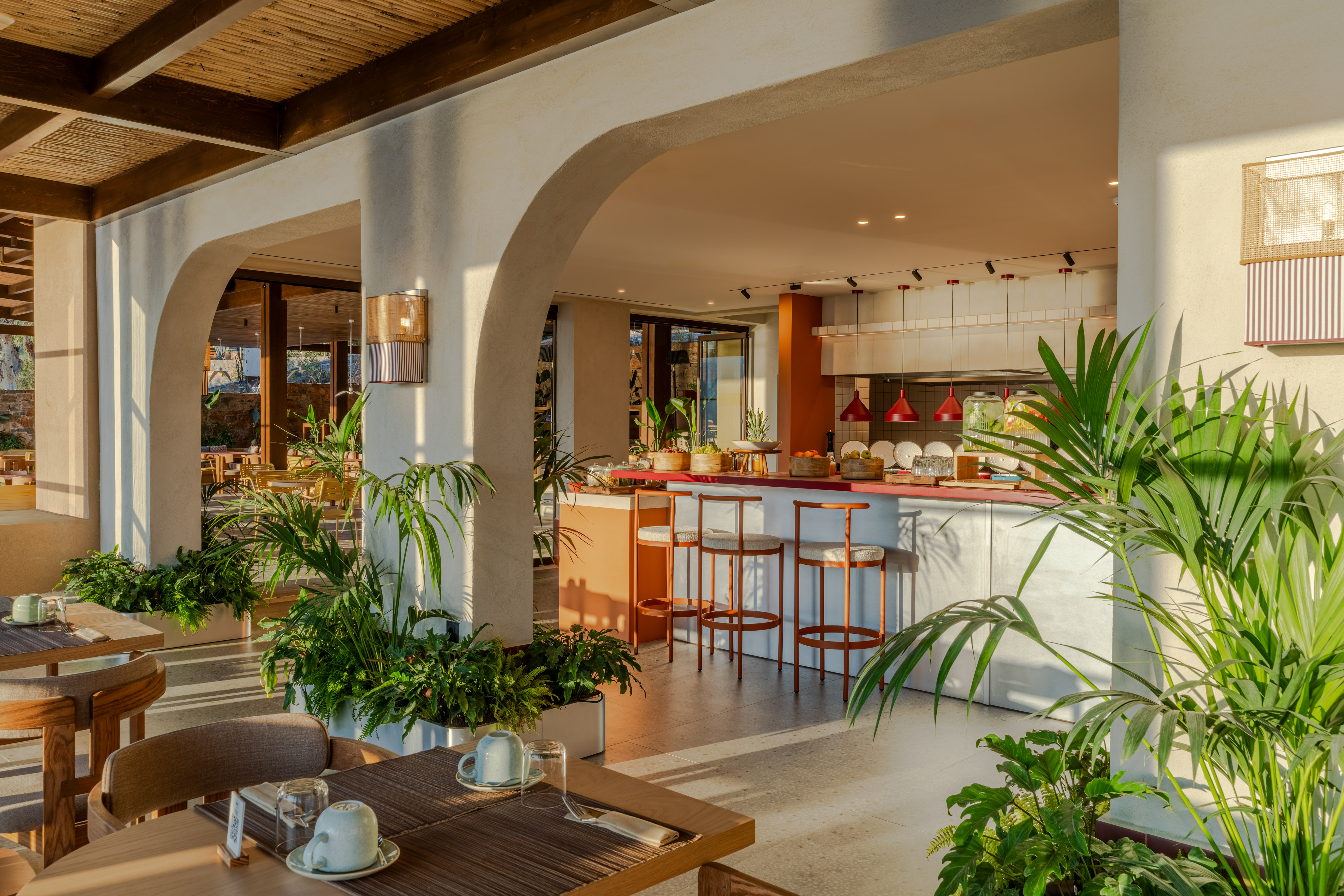 Sunny restaurant interior with breakfast bar, arches, and lush plants.