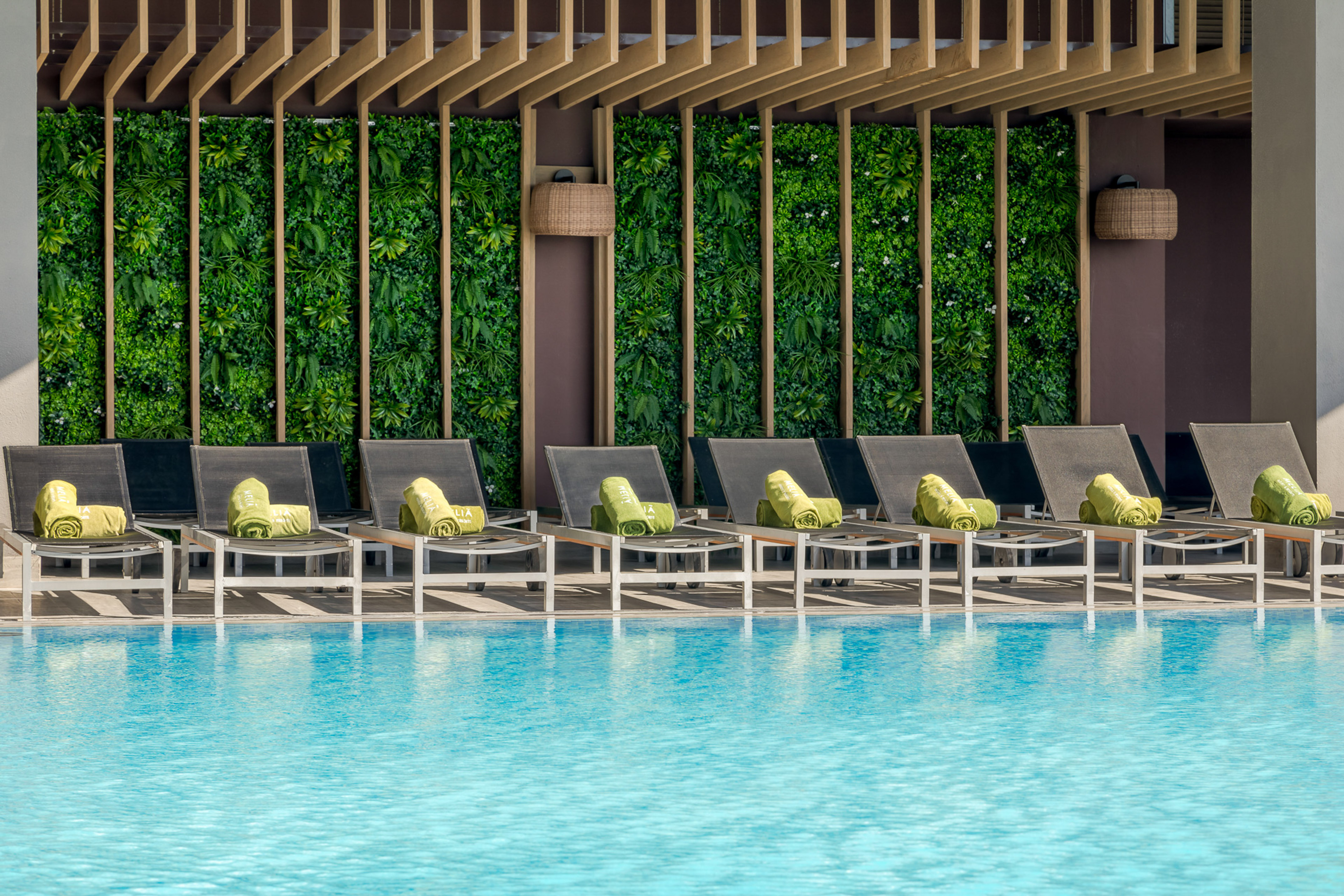 Resort pool deck with lounge chairs, green towels, and living wall.