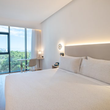 a bed with a white cover and a desk and a chair in a room with windows