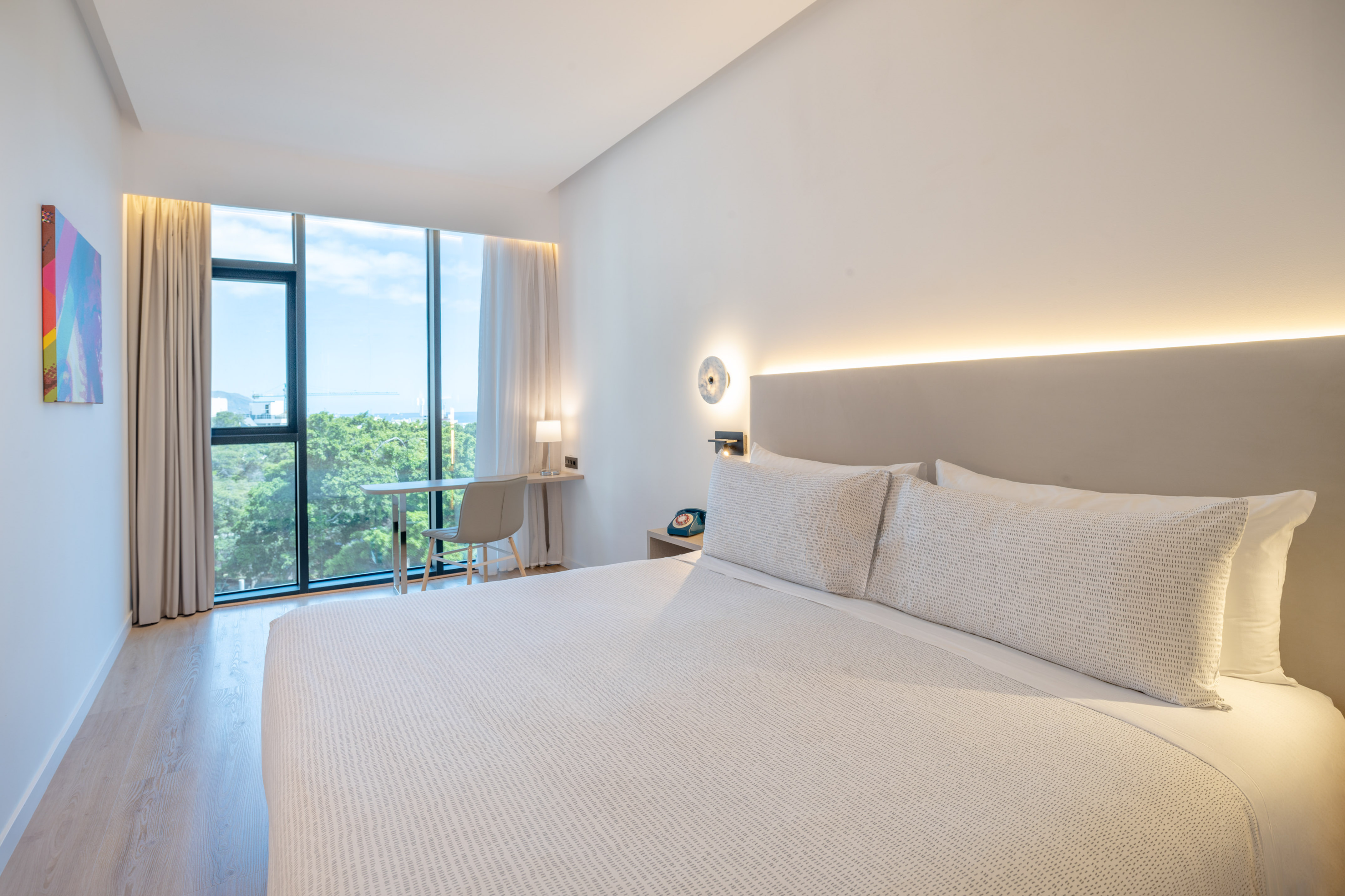 Bright modern hotel room with large window, green landscape view, and desk.