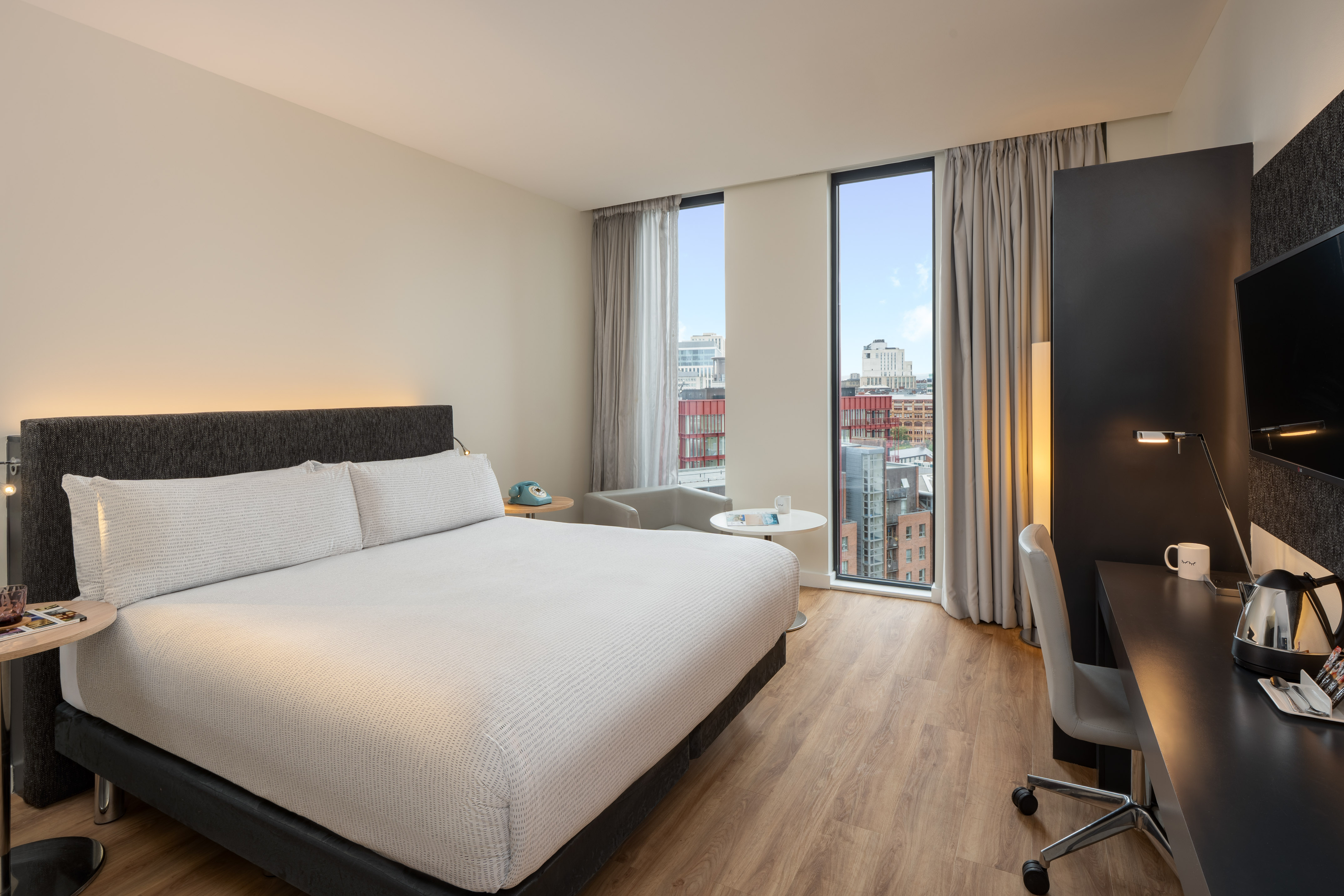 Contemporary hotel room with king bed, city views, and dedicated workspace.