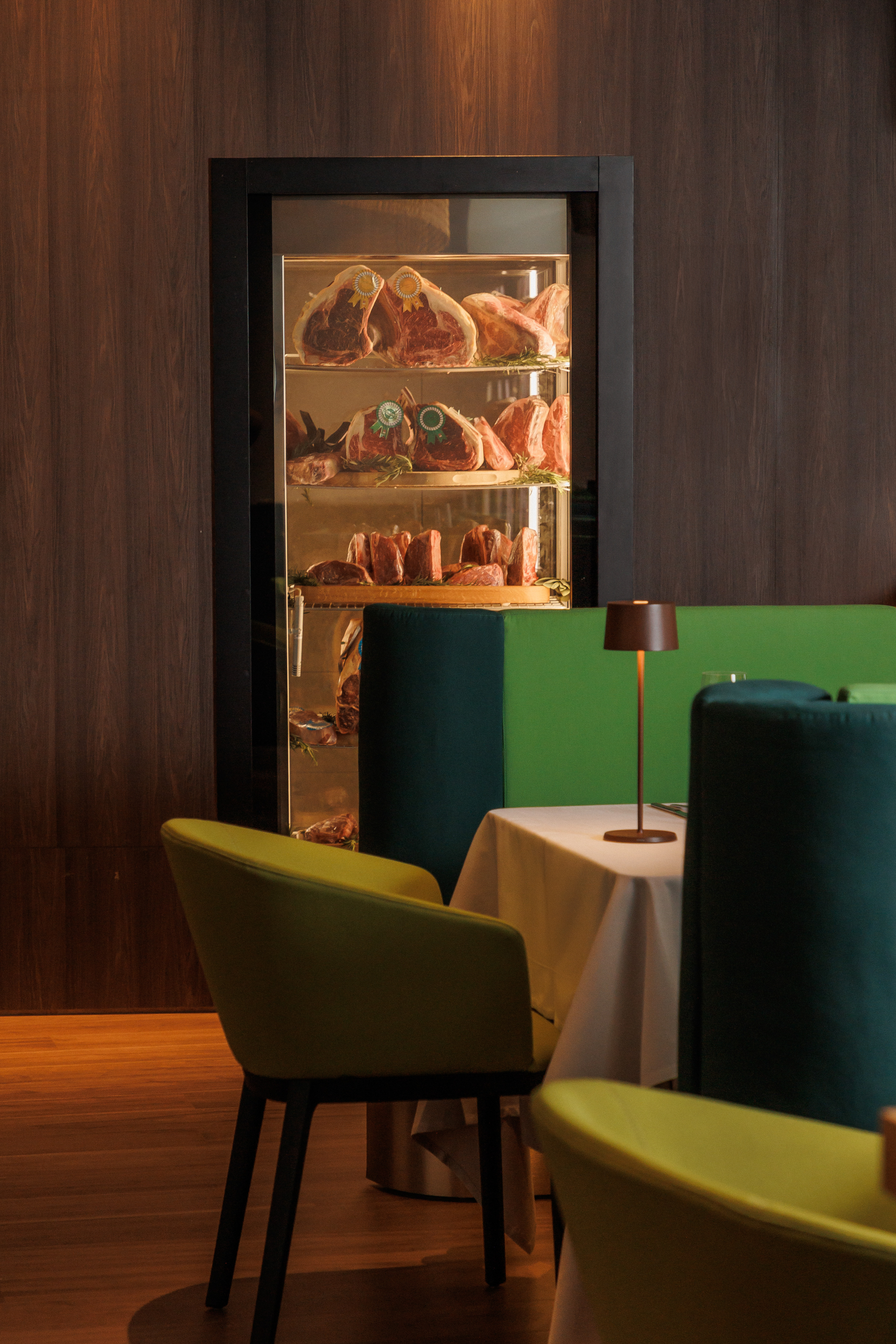 Dry-aged steak display in a modern restaurant with green seating and wooden accents.