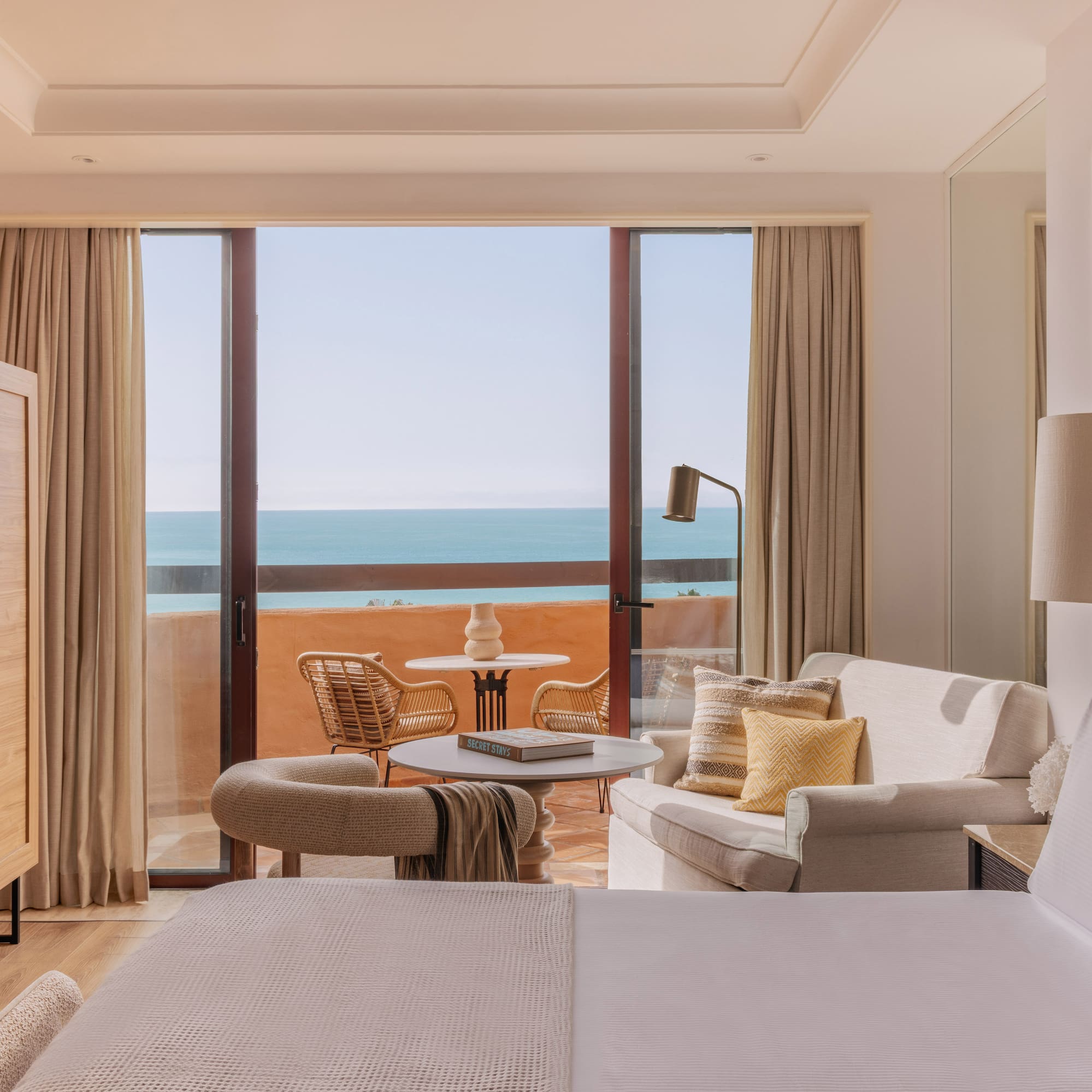 Beachfront resort room with ocean view balcony, seating area, and bed.