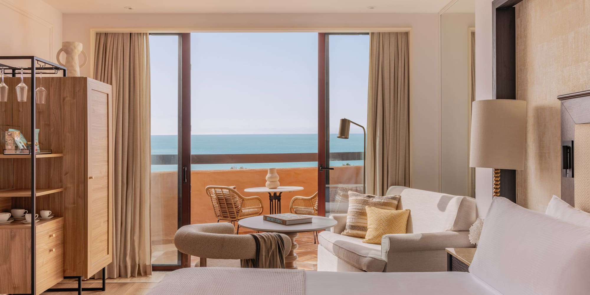 Beachfront resort room with ocean view balcony, seating area, and bed.
