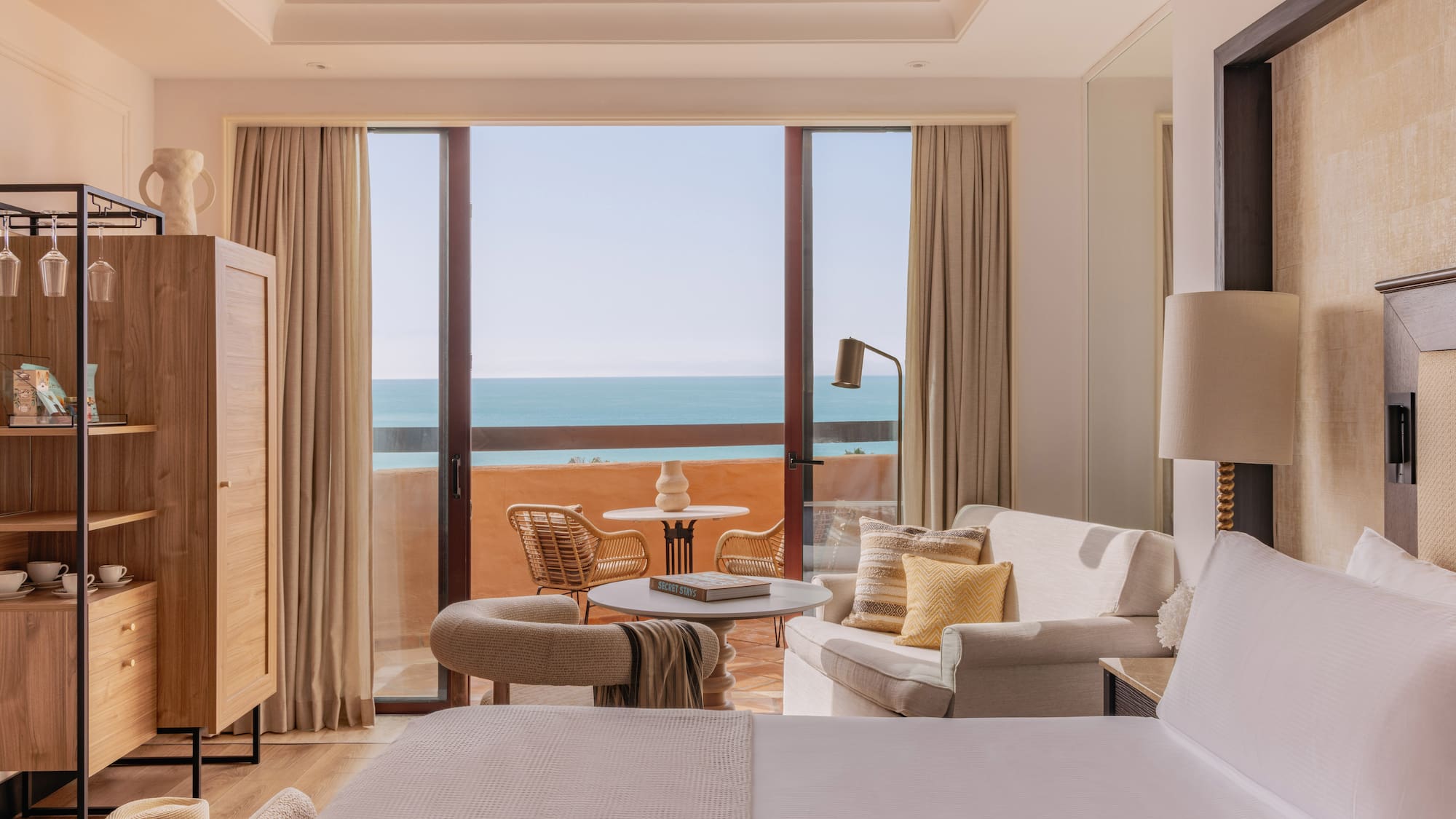 Beachfront resort room with ocean view balcony, seating area, and bed.