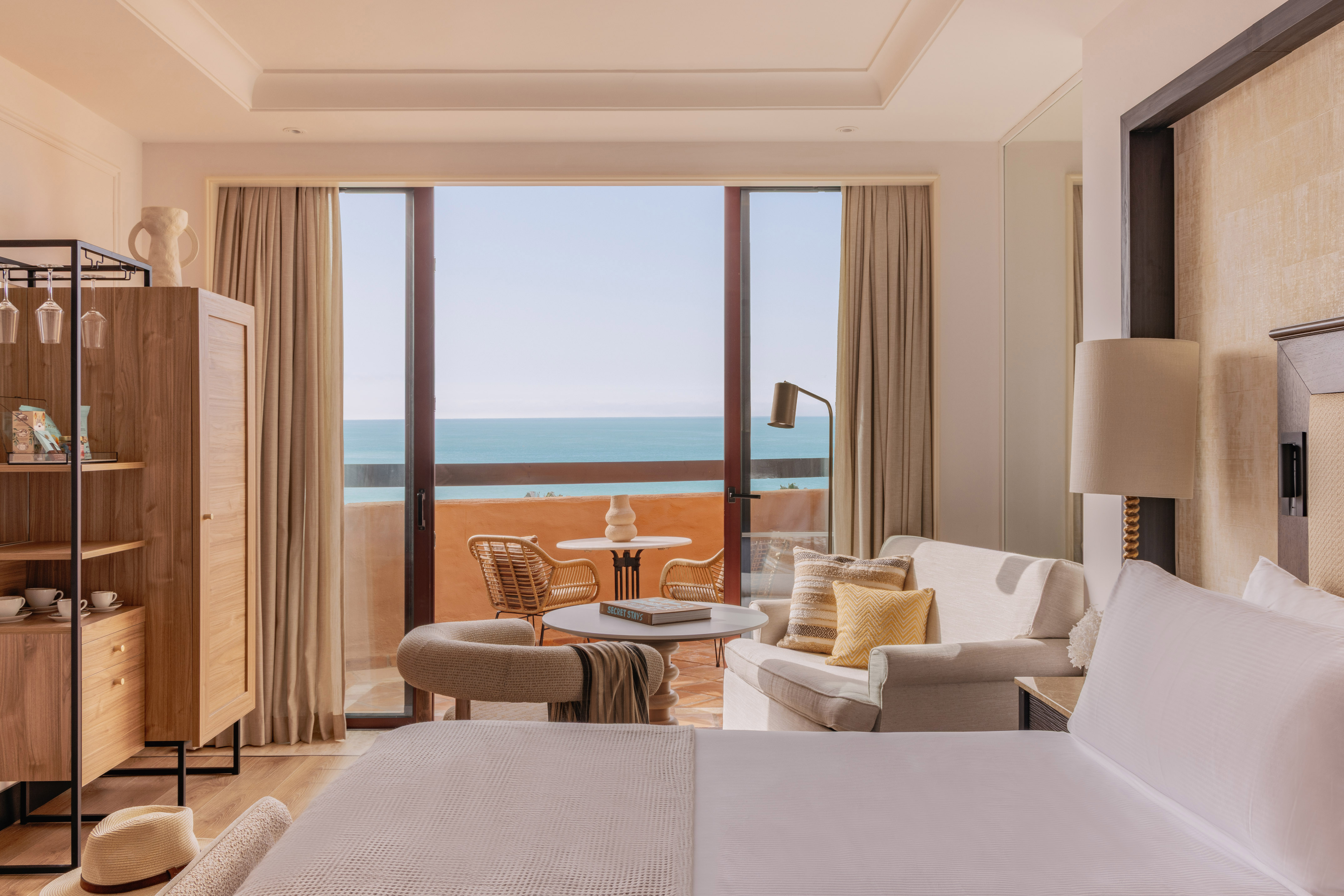 Beachfront resort room with ocean view balcony, seating area, and bed.
