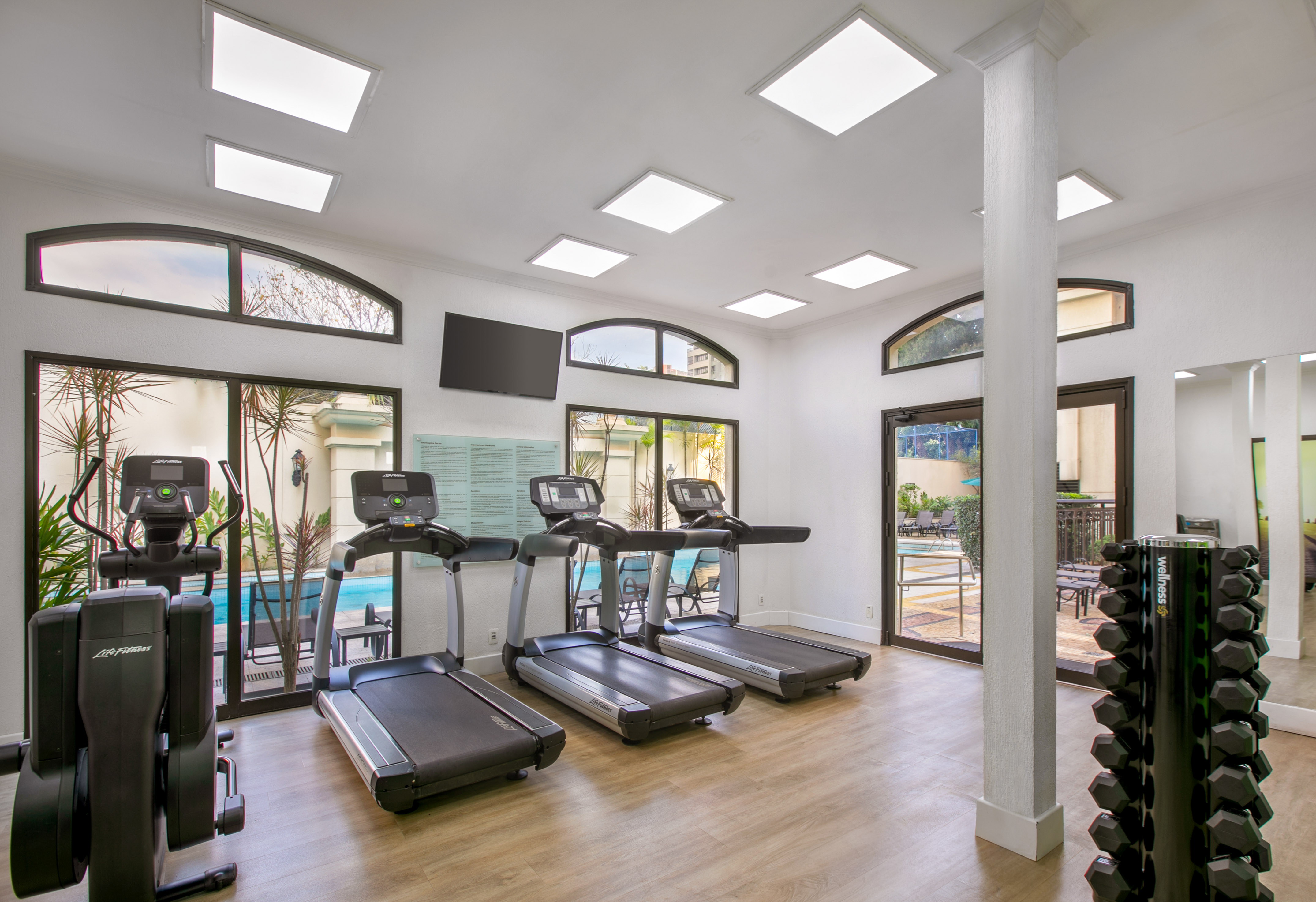 Hotel gym with treadmills, elliptical, dumbbells, and pool view access. - Meliá Campinas, Кампинас