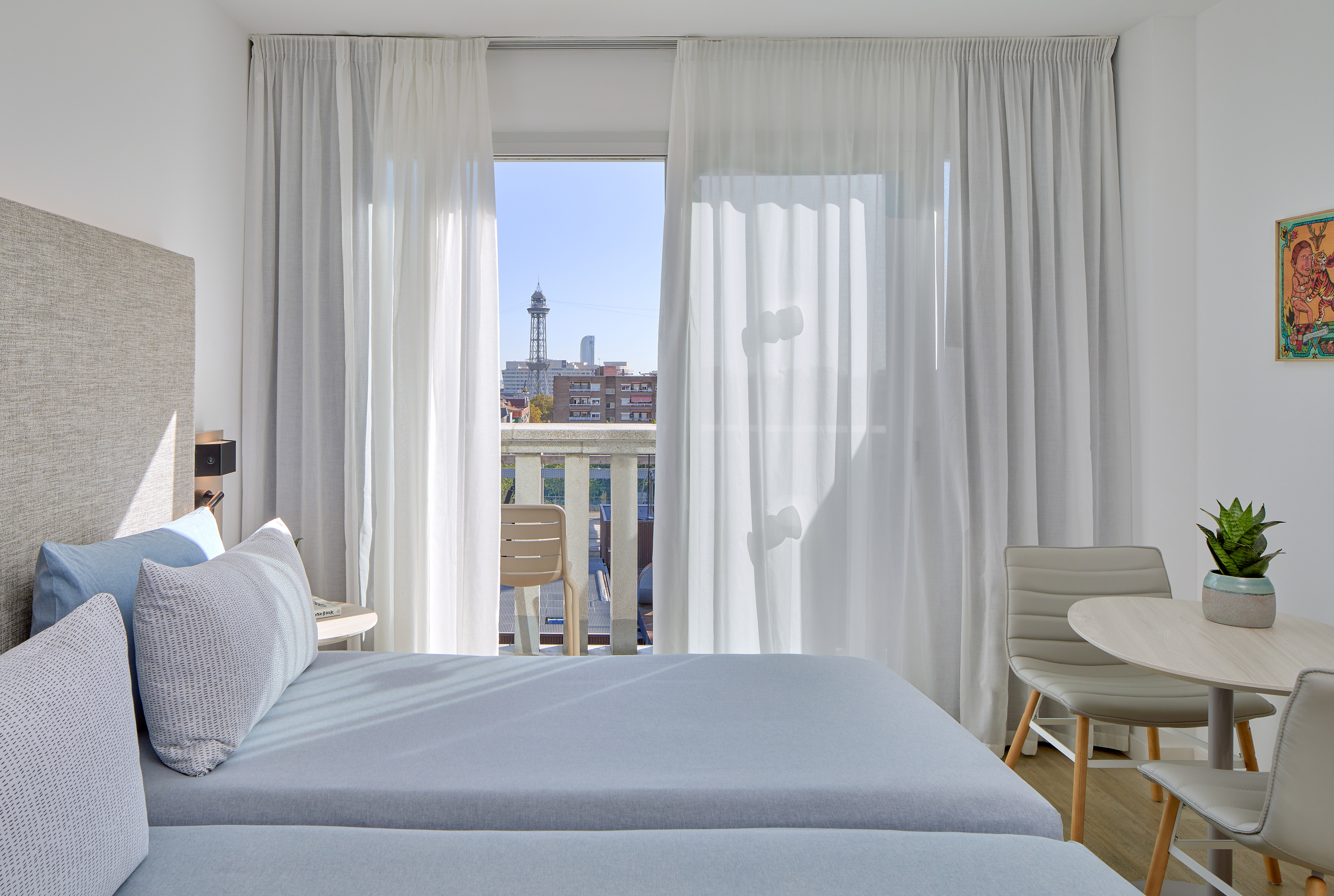 Bright hotel bedroom with twin beds, city tower view from balcony.