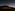 Dark car on road under vast starry night sky, large volcanic mountain in background.