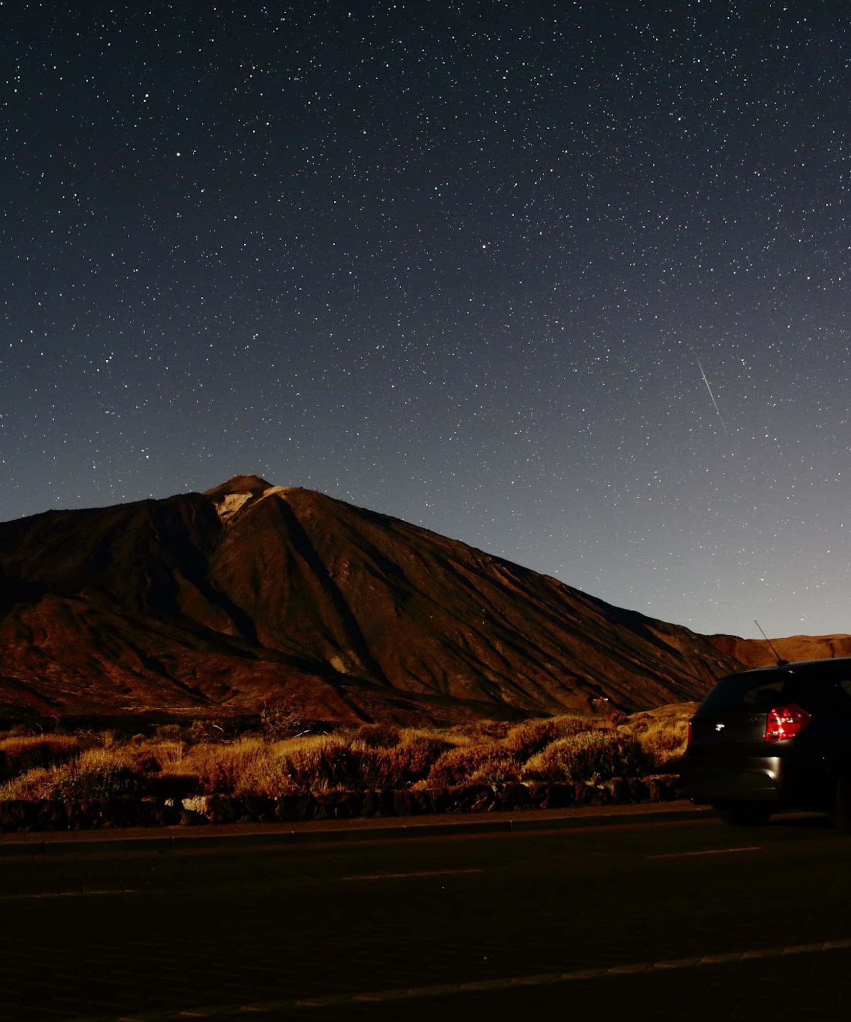 Coche bajo cielo estrellado con volcán Teide de noche en Canarias.