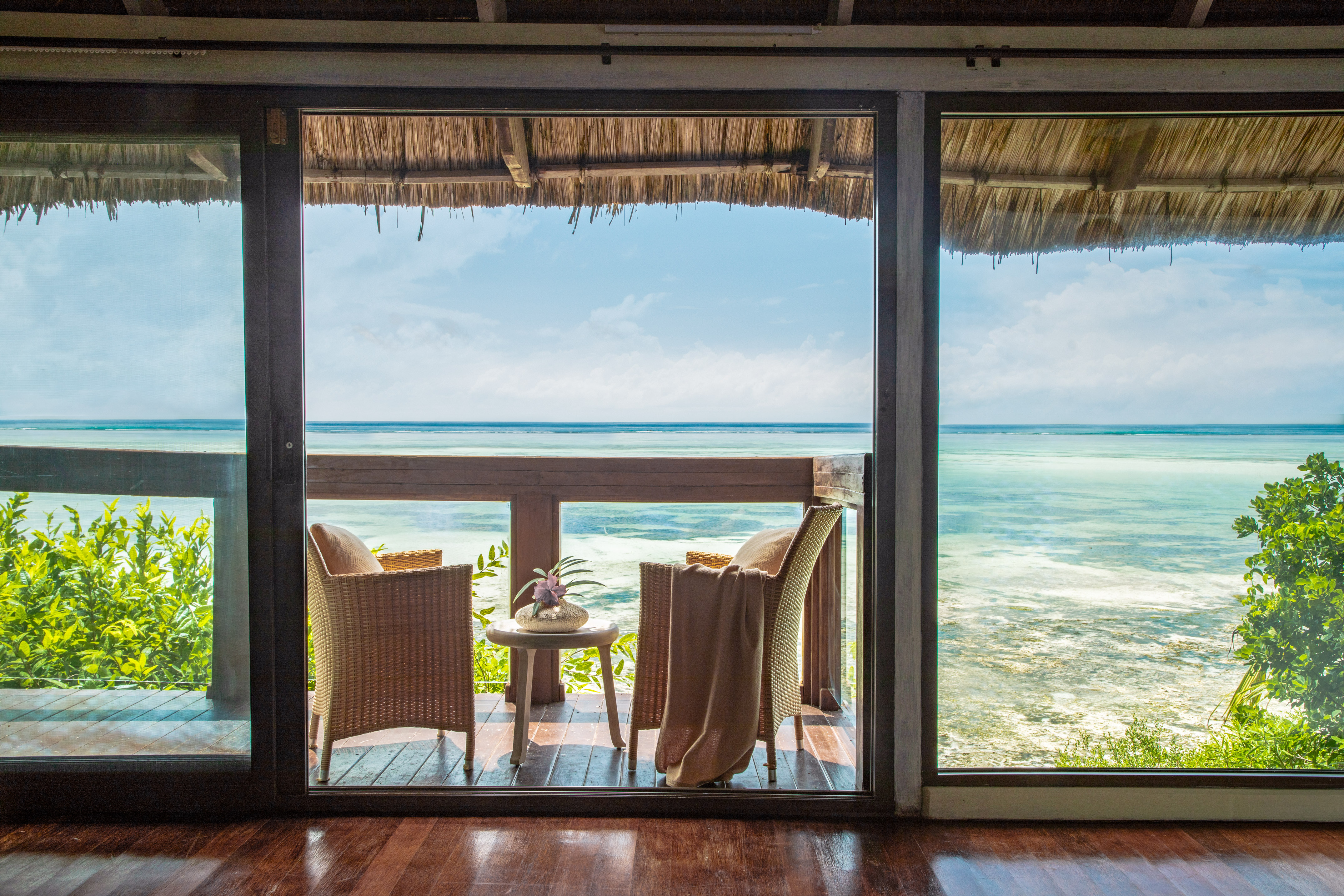 Tropical beachfront balcony with rattan chairs and serene ocean view.