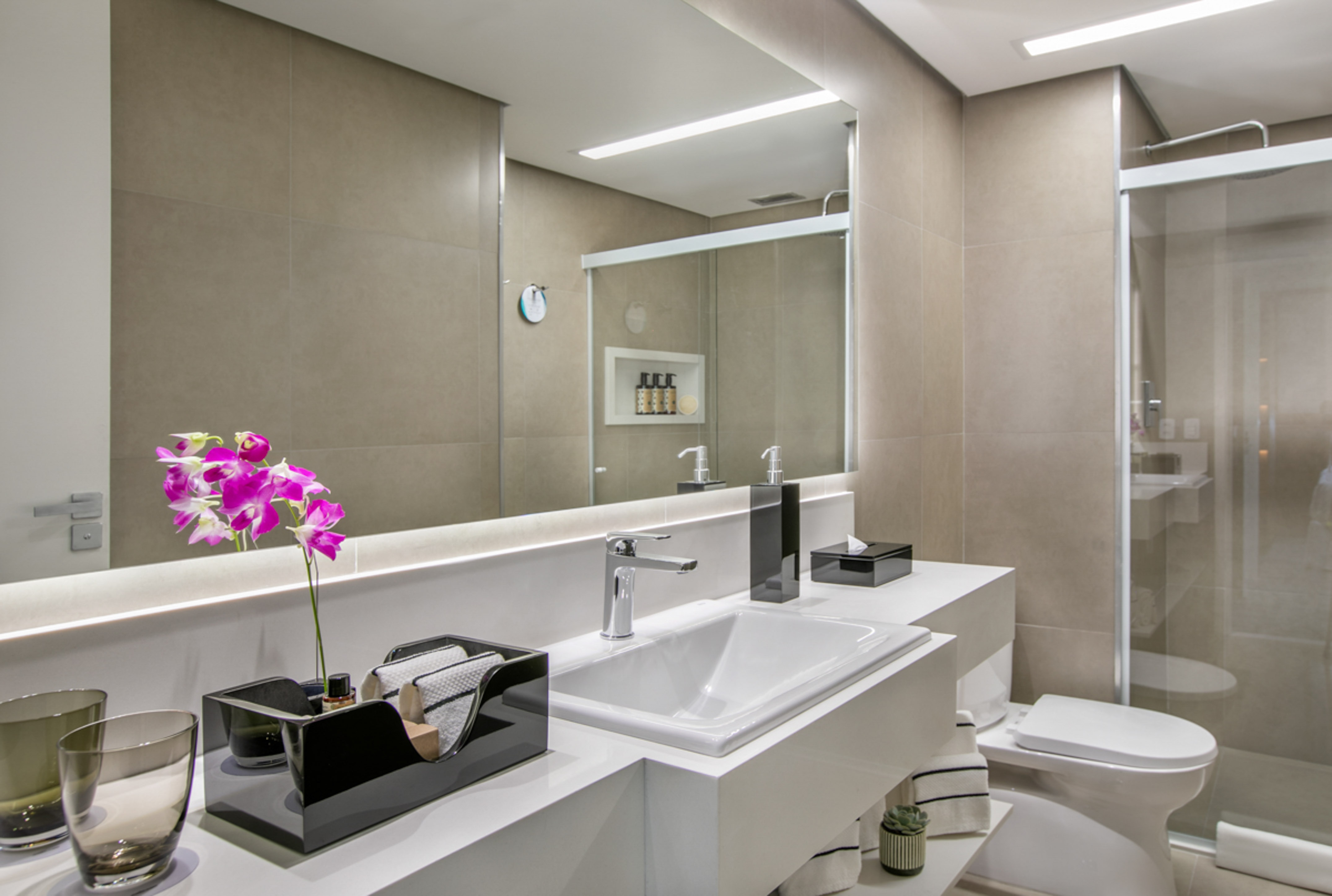 Modern bathroom with white vanity, sink, toilet, glass shower, and pink orchid.