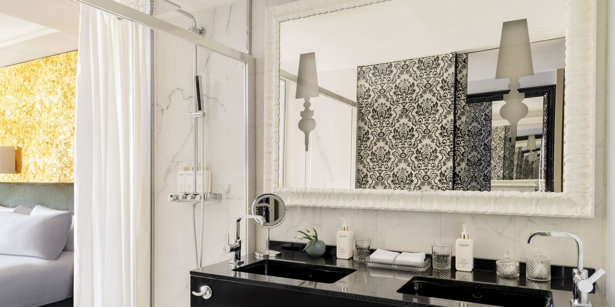 Baño de suite moderno con doble lavabo, ducha, espejo y dormitorio.