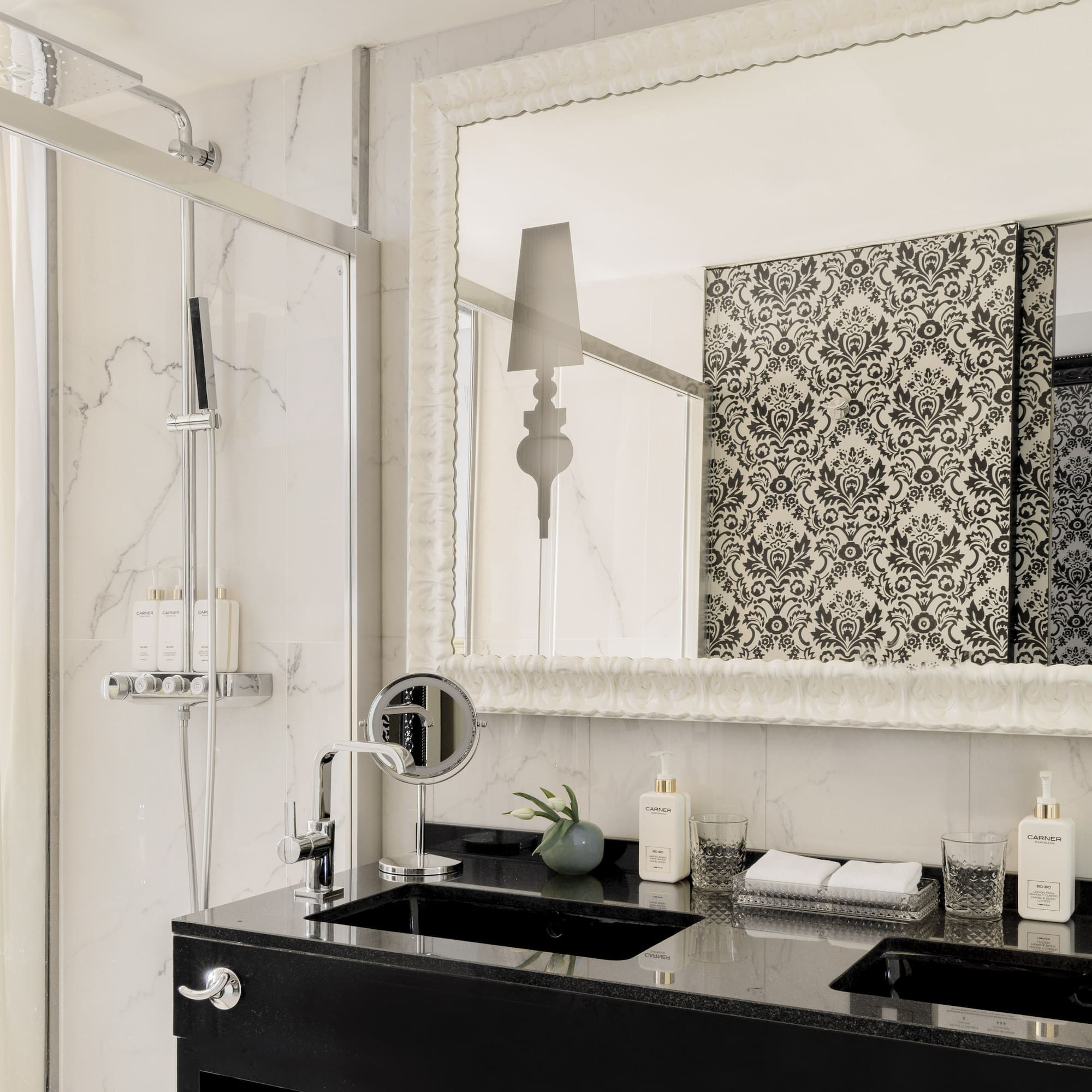 Baño de suite moderno con doble lavabo, ducha, espejo y dormitorio.