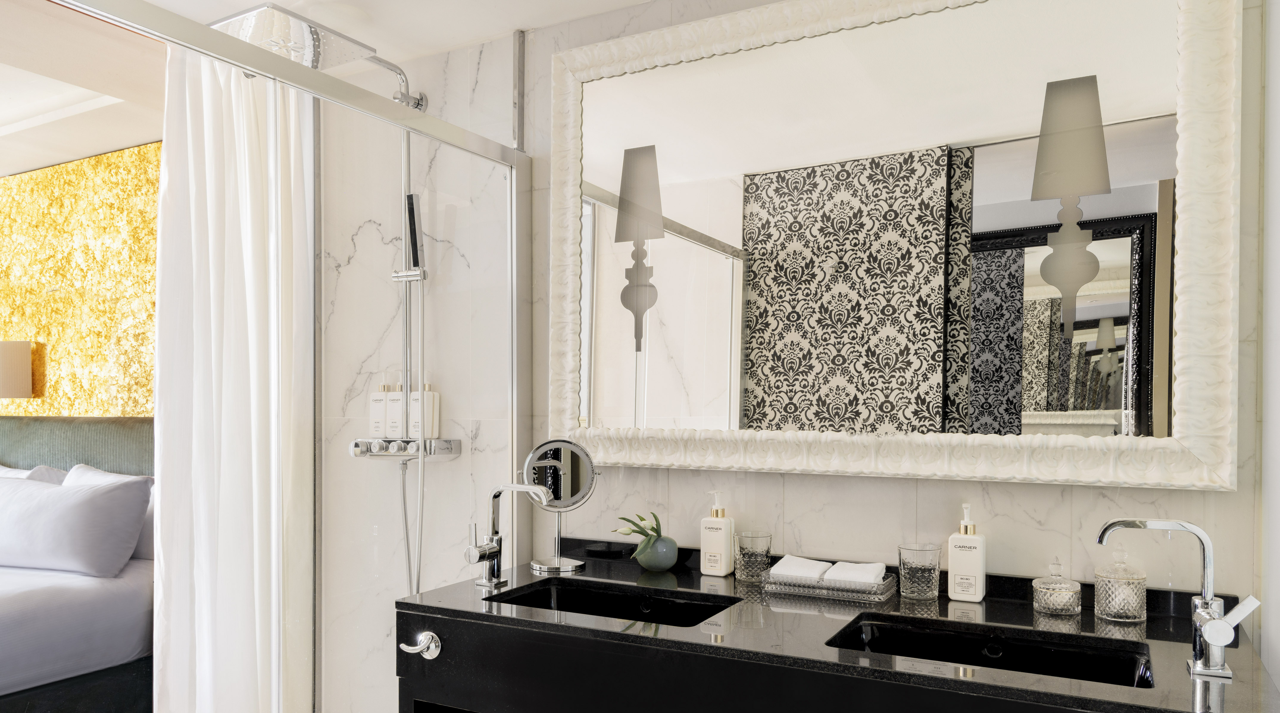 Baño de suite moderno con doble lavabo, ducha, espejo y dormitorio.