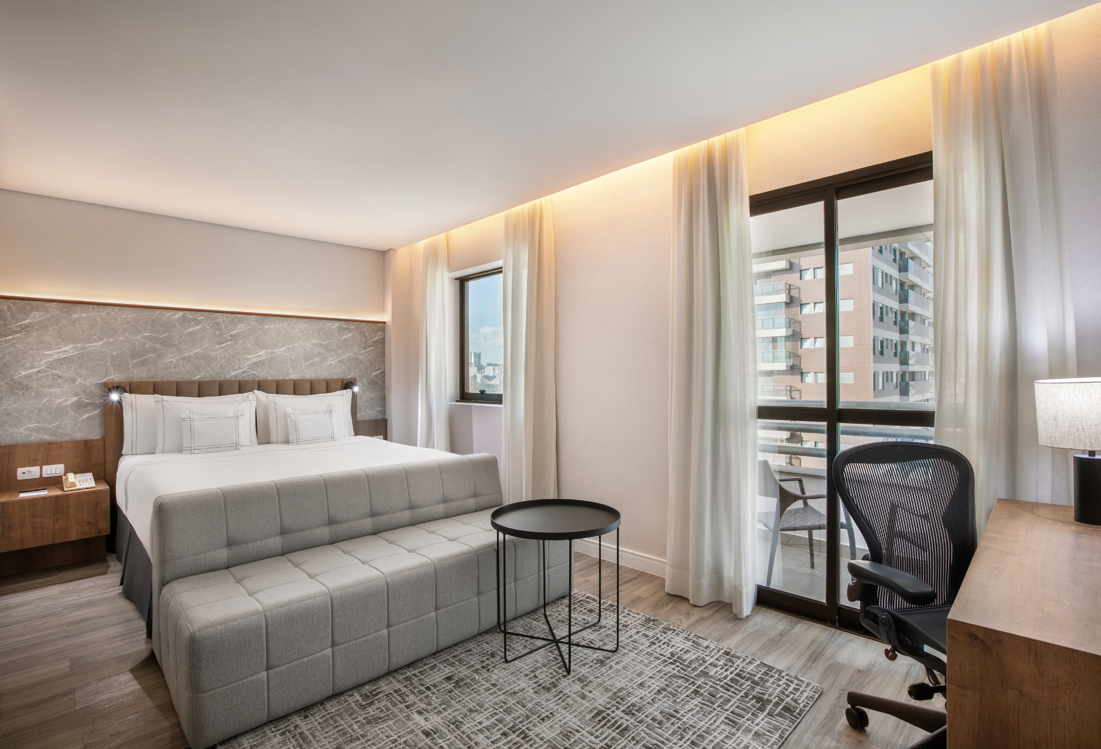Modern hotel room: king bed, desk, balcony, marble headboard.