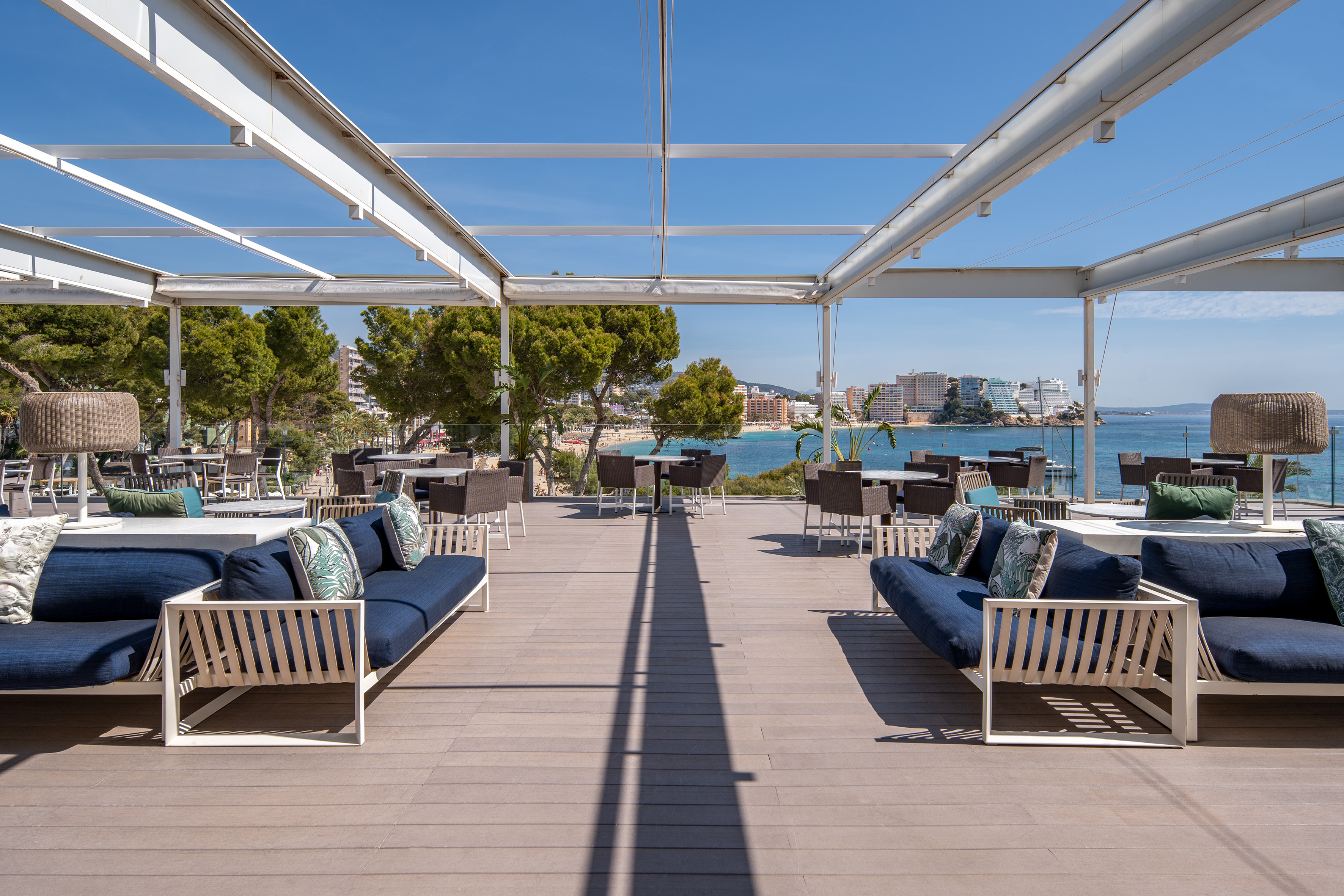Sunny outdoor restaurant terrace with modern seating and ocean views.