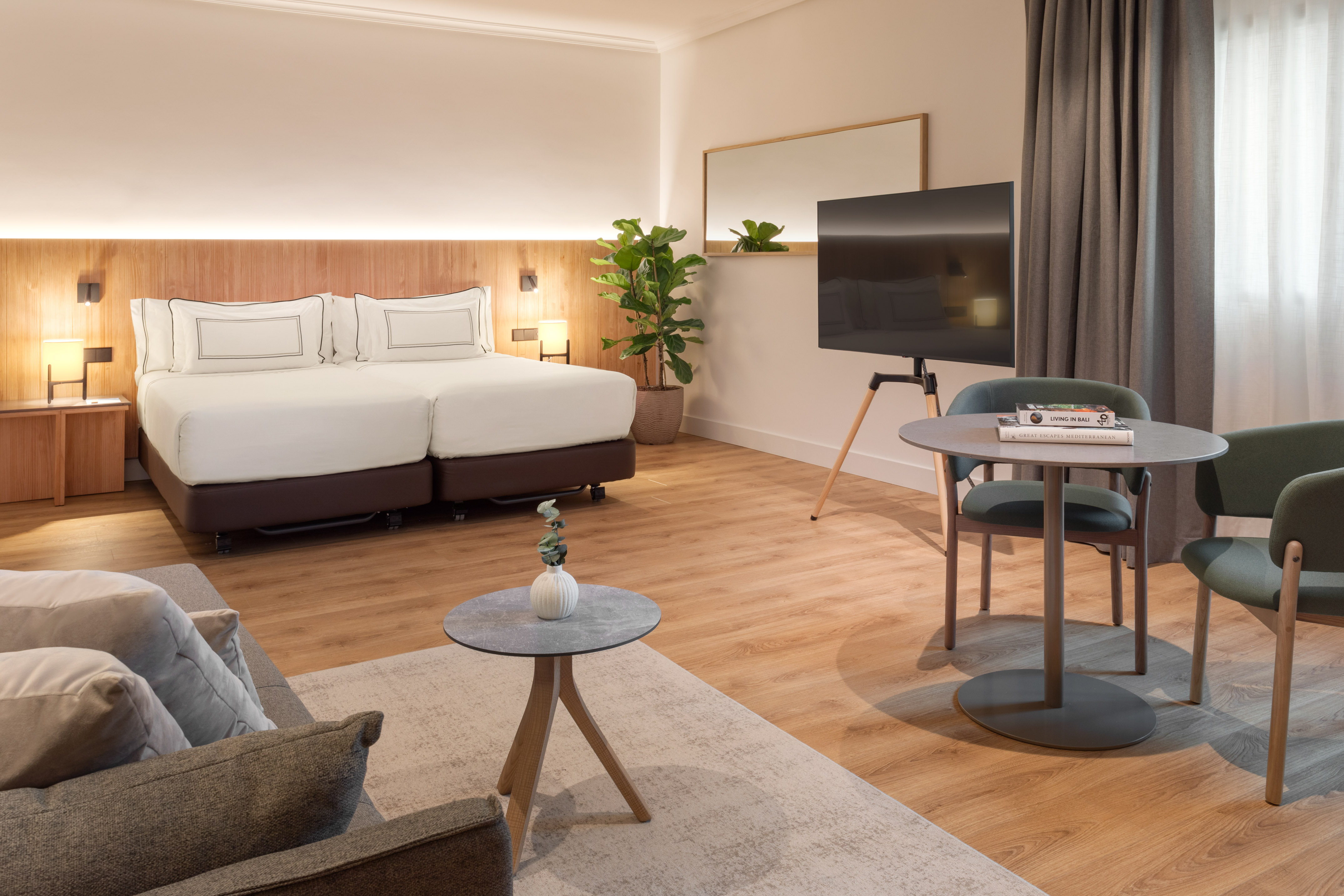 Modern hotel room with twin beds, living and dining area, and flat-screen TV.
