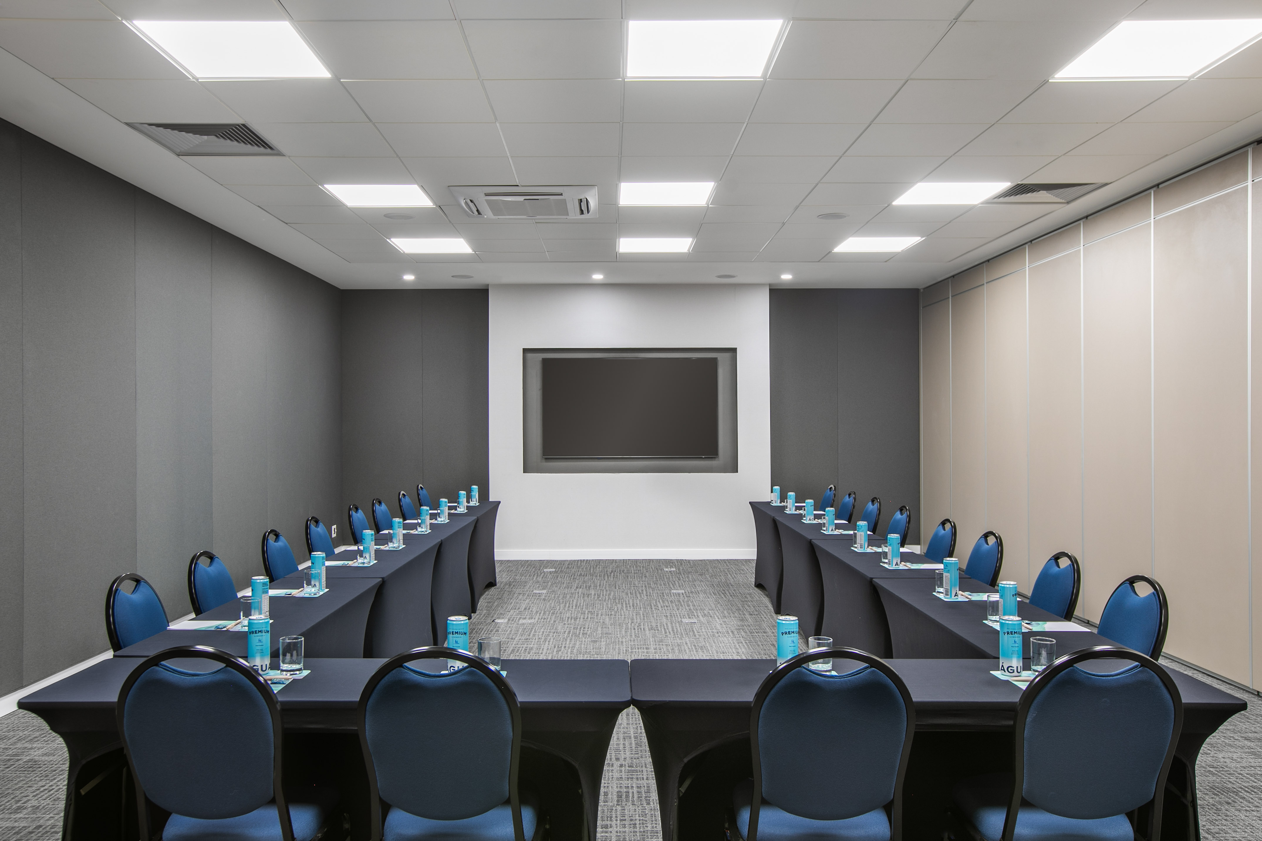 U-shape conference room with large TV, blue chairs, and refreshments.