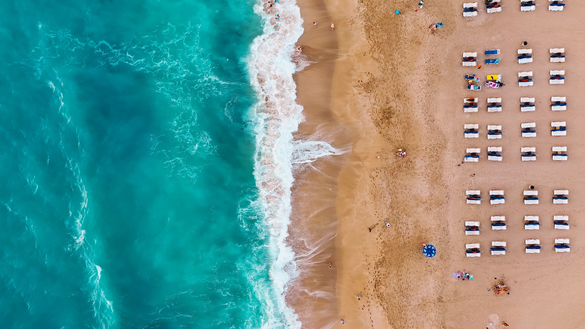 Aerial view: tropical sandy beach, turquoise ocean waves, sun loungers.